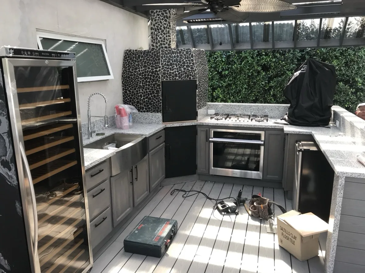 An outdoor kitchen with a stone pizza oven and wine fridge nearing completion on a Trex deck