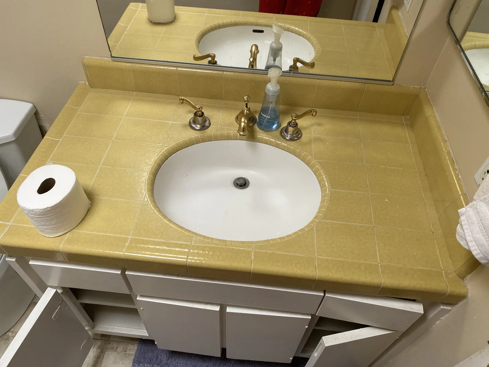 A close view of the original tile countertop with an oval sink and gold double-handle faucet