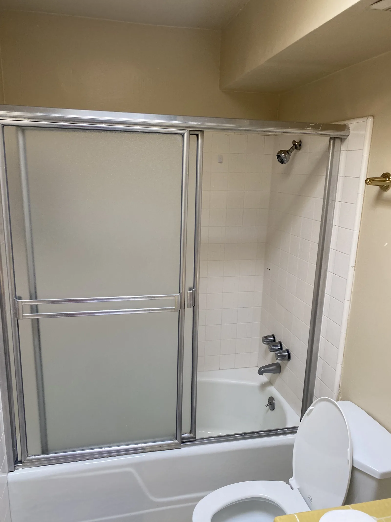 The original tub and shower with white subway tile and a sliding glass door, dropped ceiling visible above