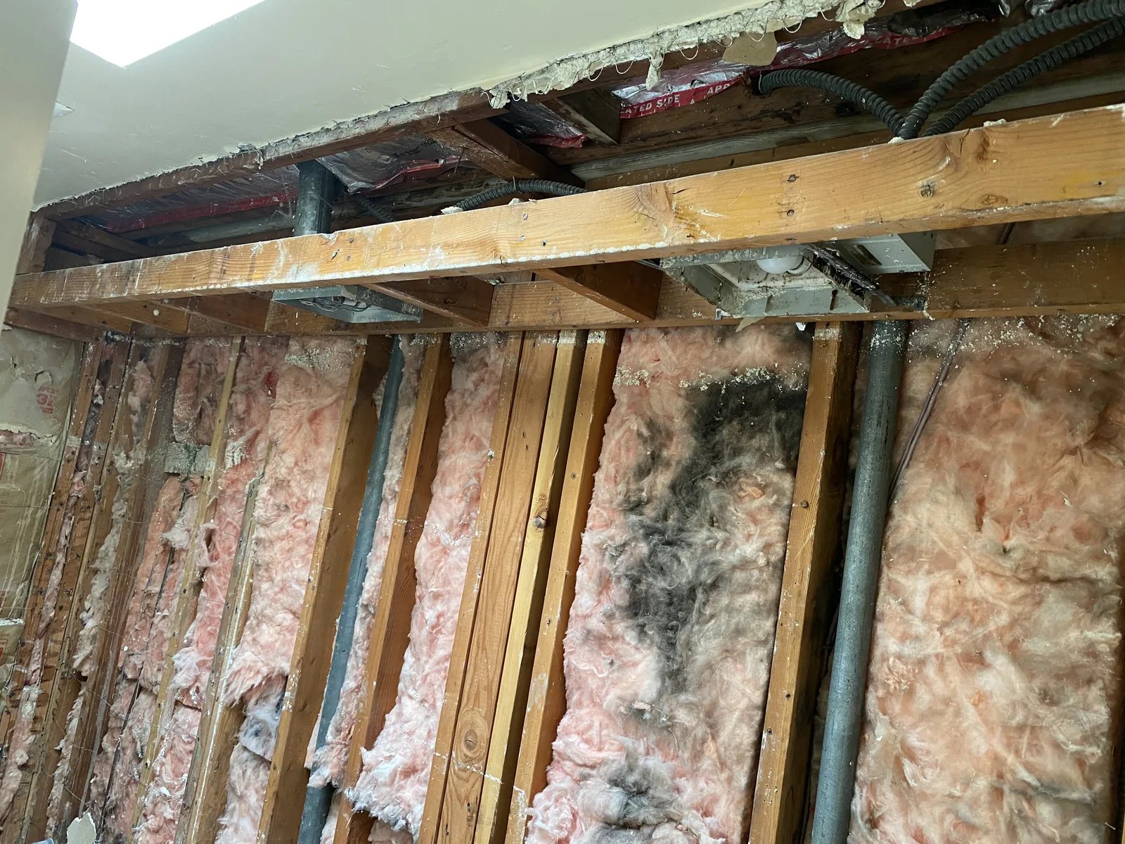 A ceiling soffit opened up, exposing old insulation, wiring, and the original skylight opening