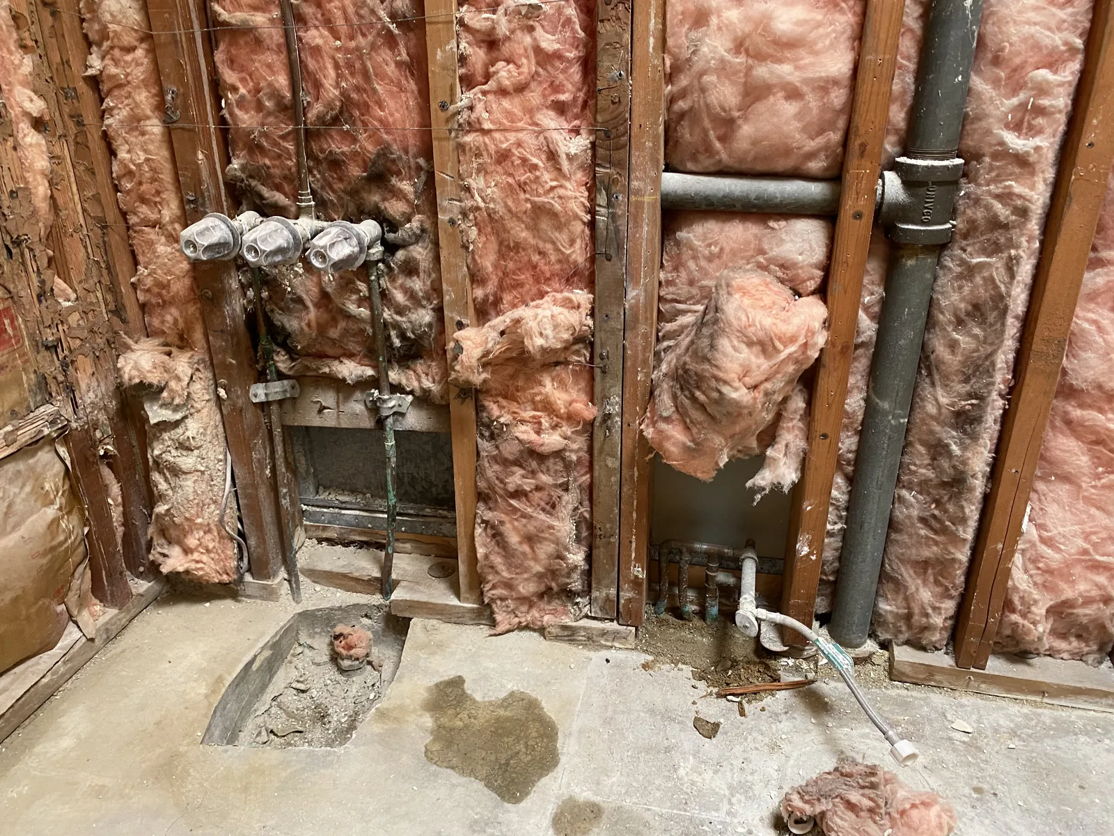 The concrete slab cut open on the bathroom floor, with the old shower valve rough-in exposed in the wall