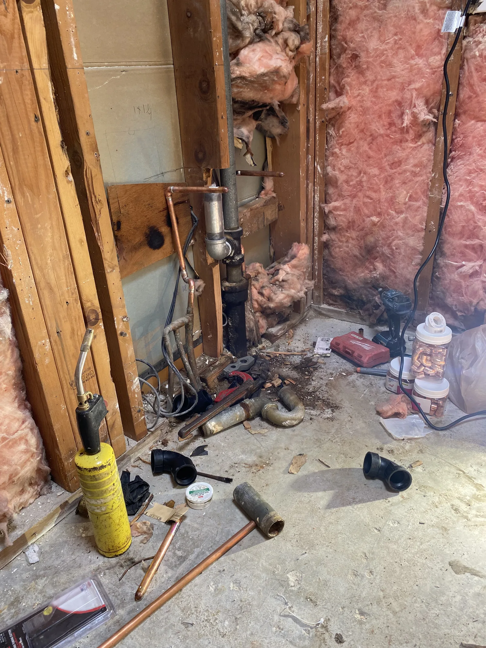 A plumber sweating copper pipe fittings with a torch, with the cast iron waste stack exposed in the open wall