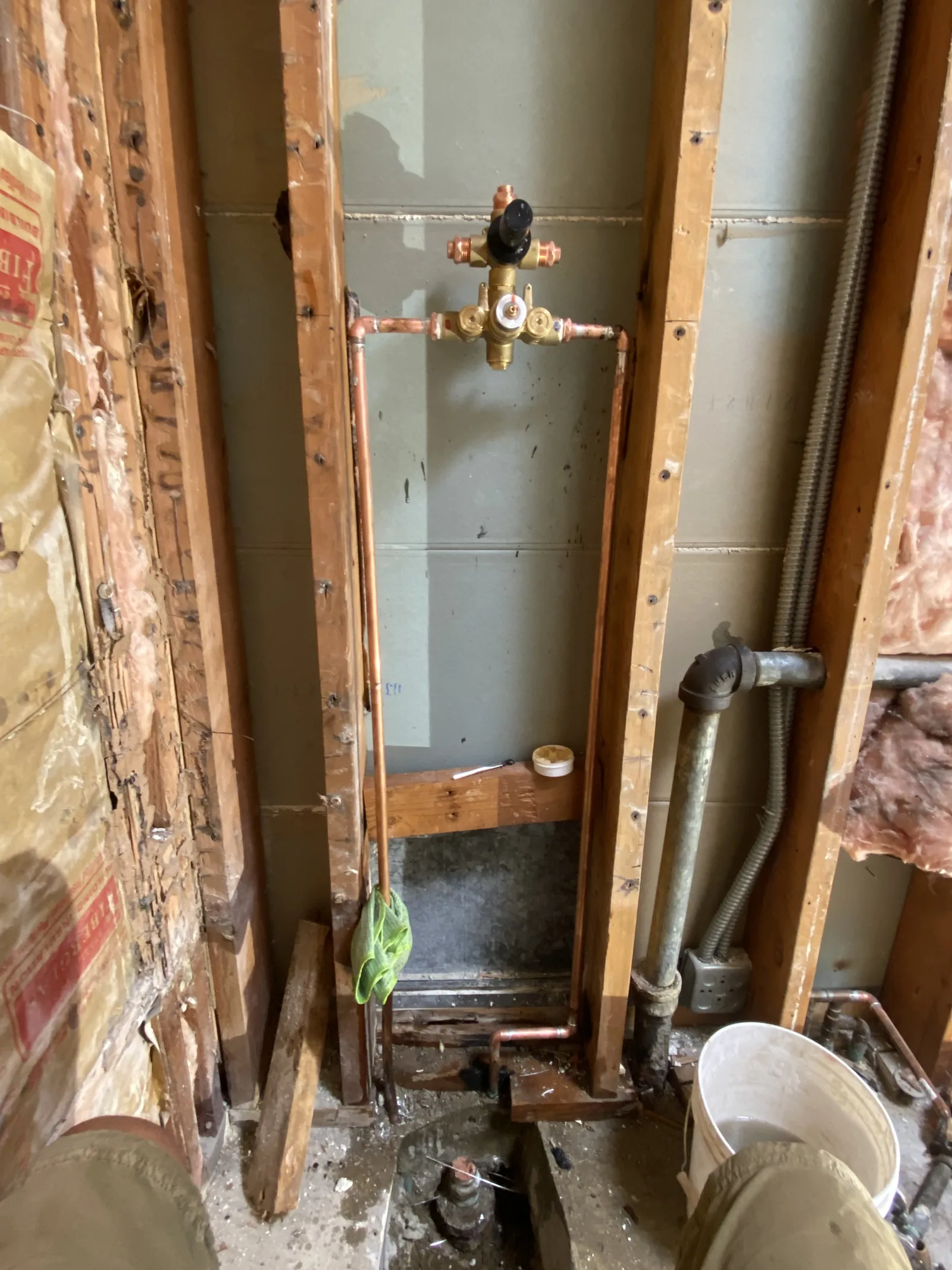 A new brass shower mixing valve installed on copper pipe runs inside an open stud wall