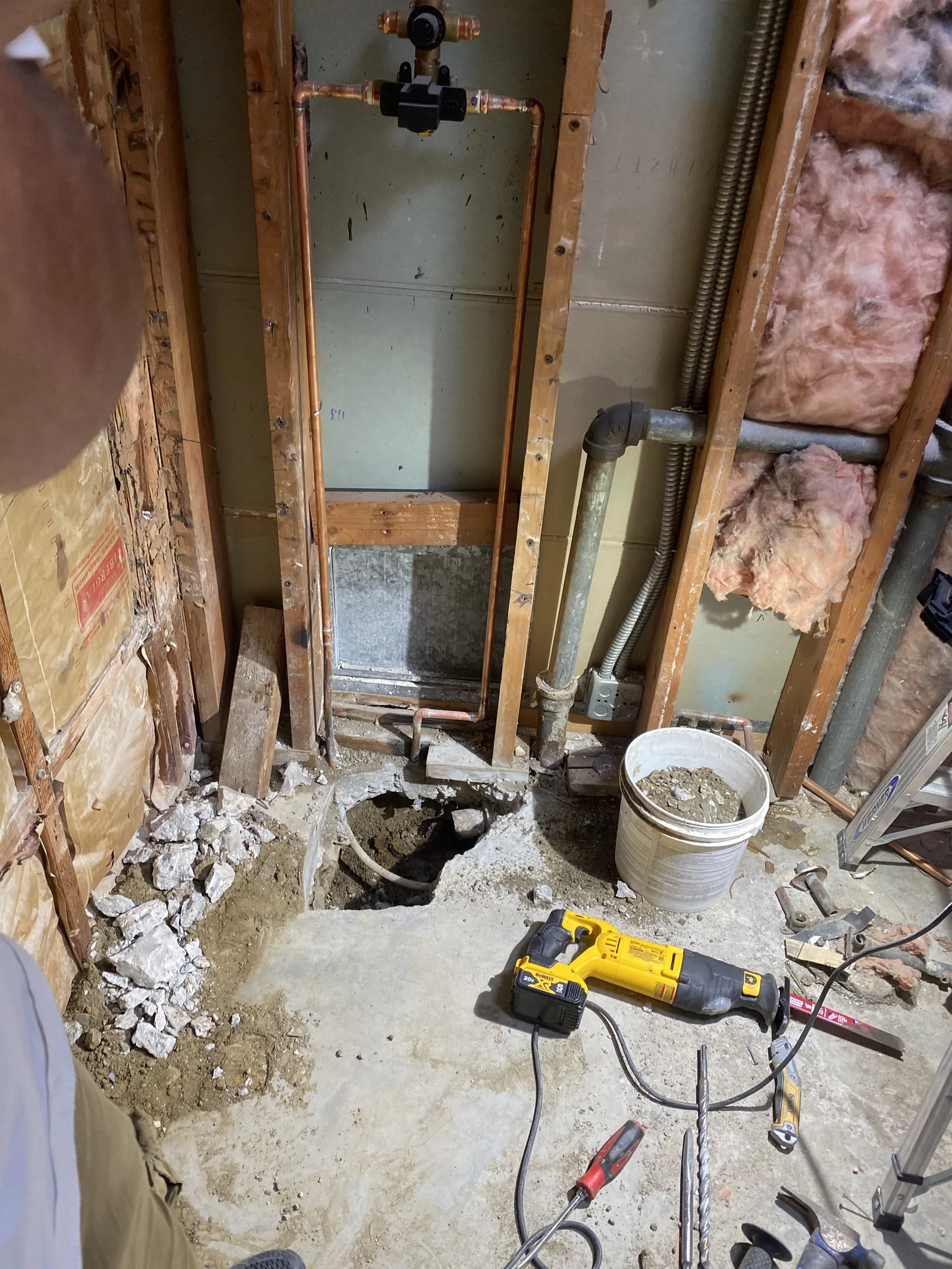 A freshly cut section of concrete slab with rubble, a reciprocating saw, and tools scattered around it