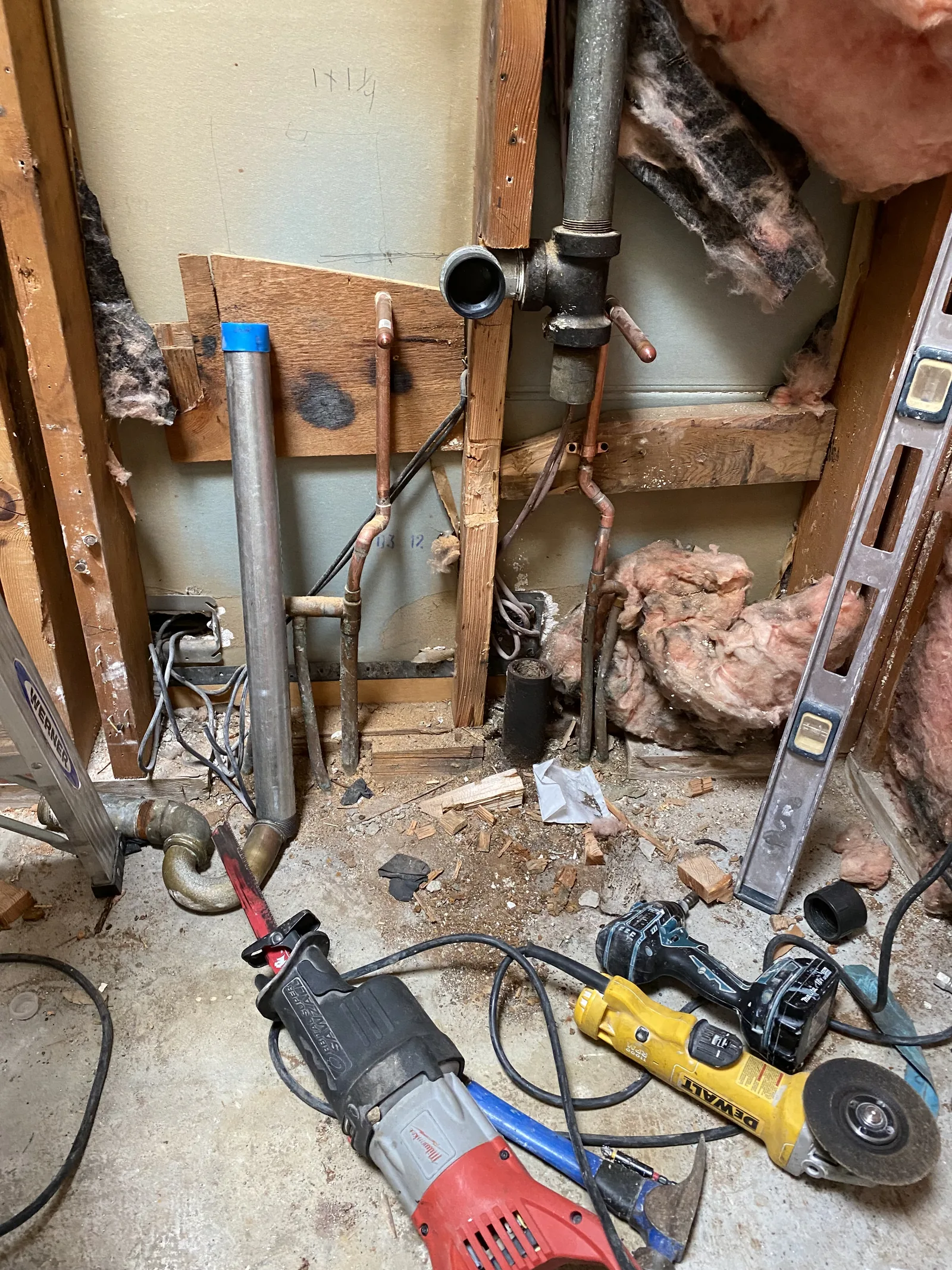 A galvanized vent pipe and copper stub-outs exposed in an open stud wall with tools on the floor