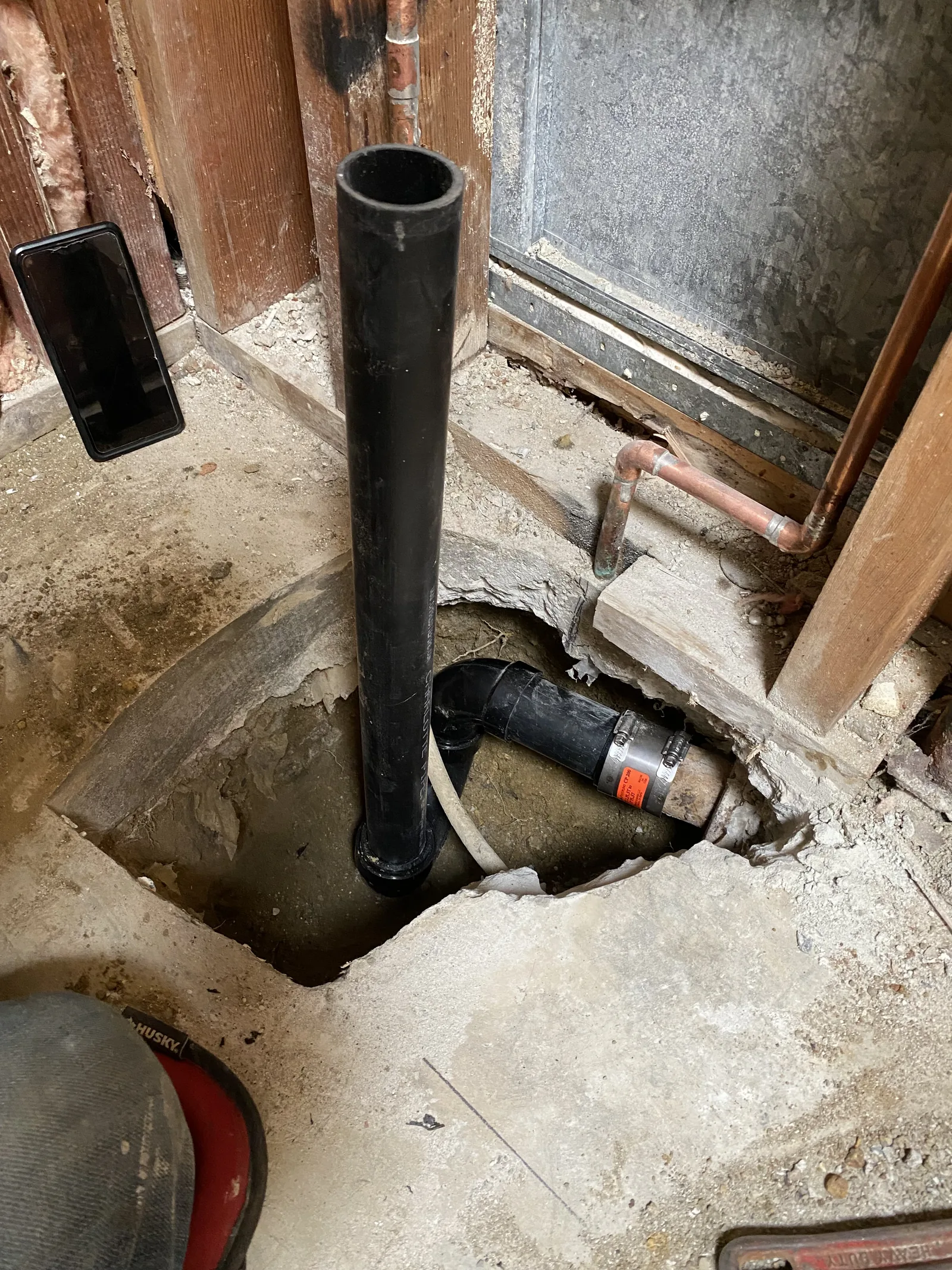 A new black ABS waste pipe connected into a cut opening in the concrete slab, tied to a coupling below