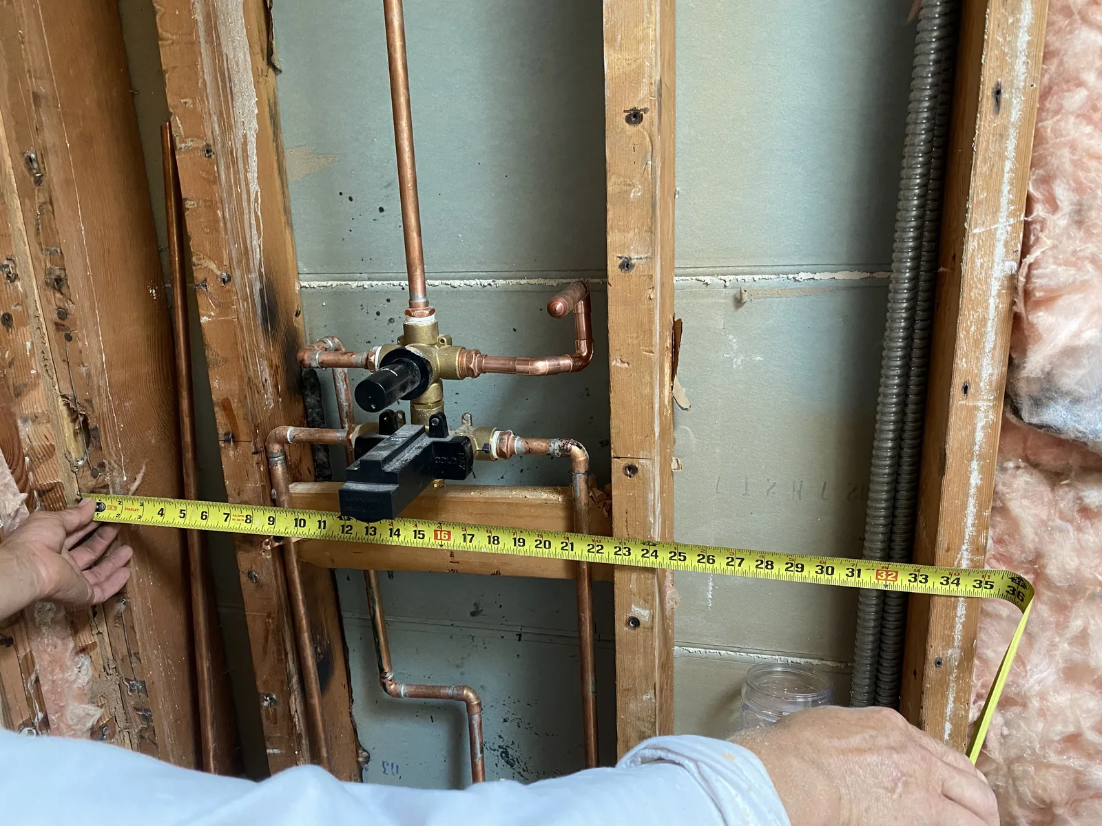 Two installers measuring the exact position for a new shower valve in an open stud wall