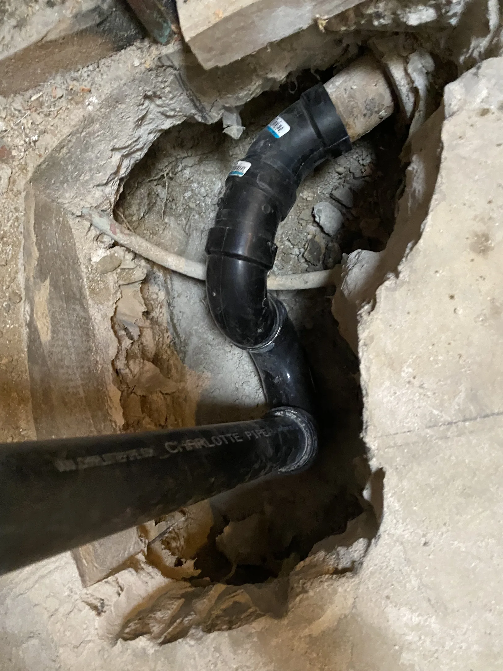 A close view of black ABS waste pipe fittings joined together inside a cut slab opening