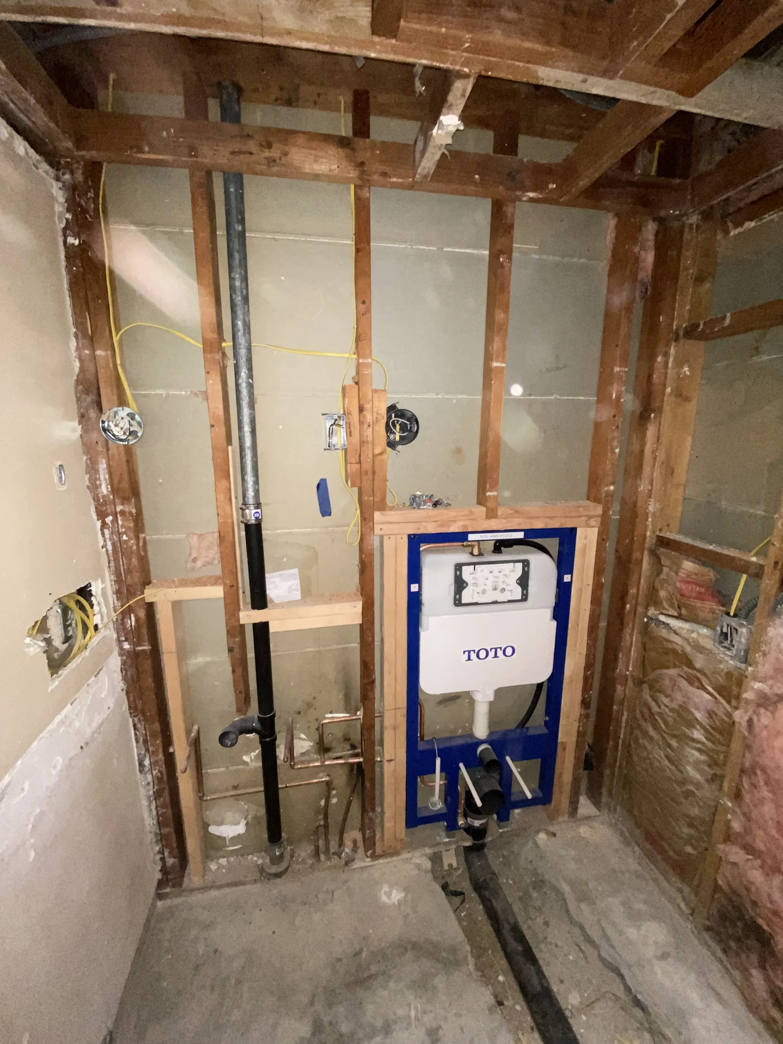 A concealed carrier frame for a wall-mounted toilet, built into the open stud wall