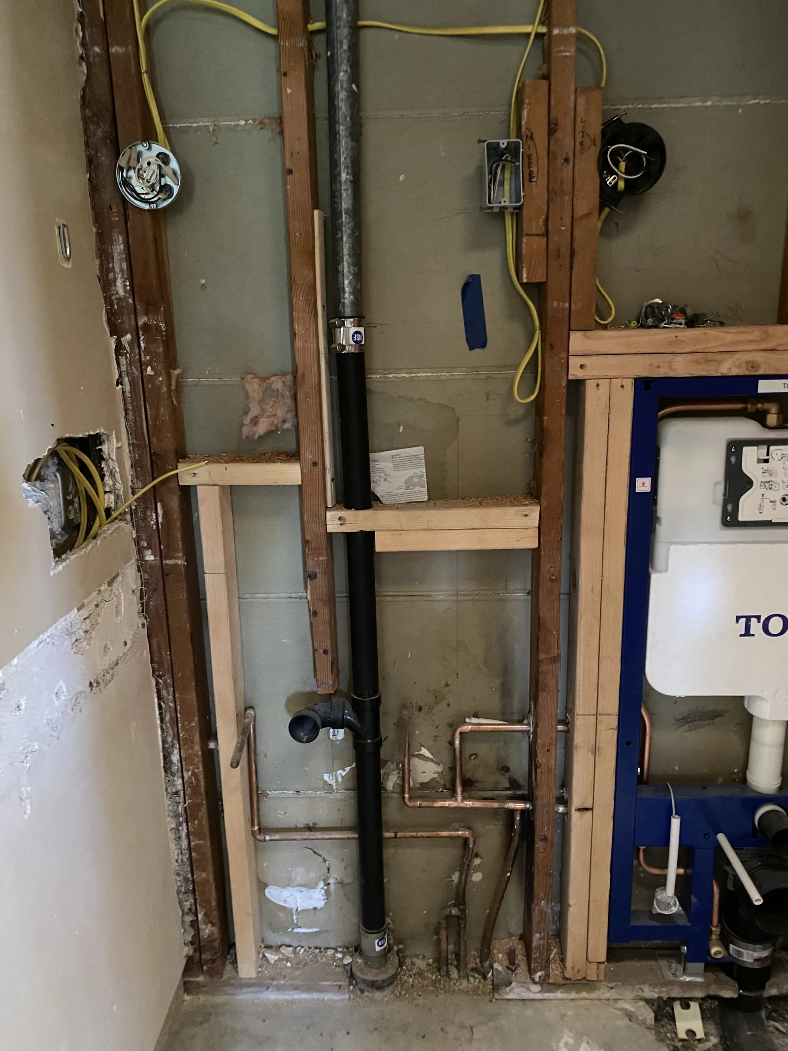 A TOTO concealed carrier frame next to electrical junction boxes and yellow low-voltage wiring in an open wall