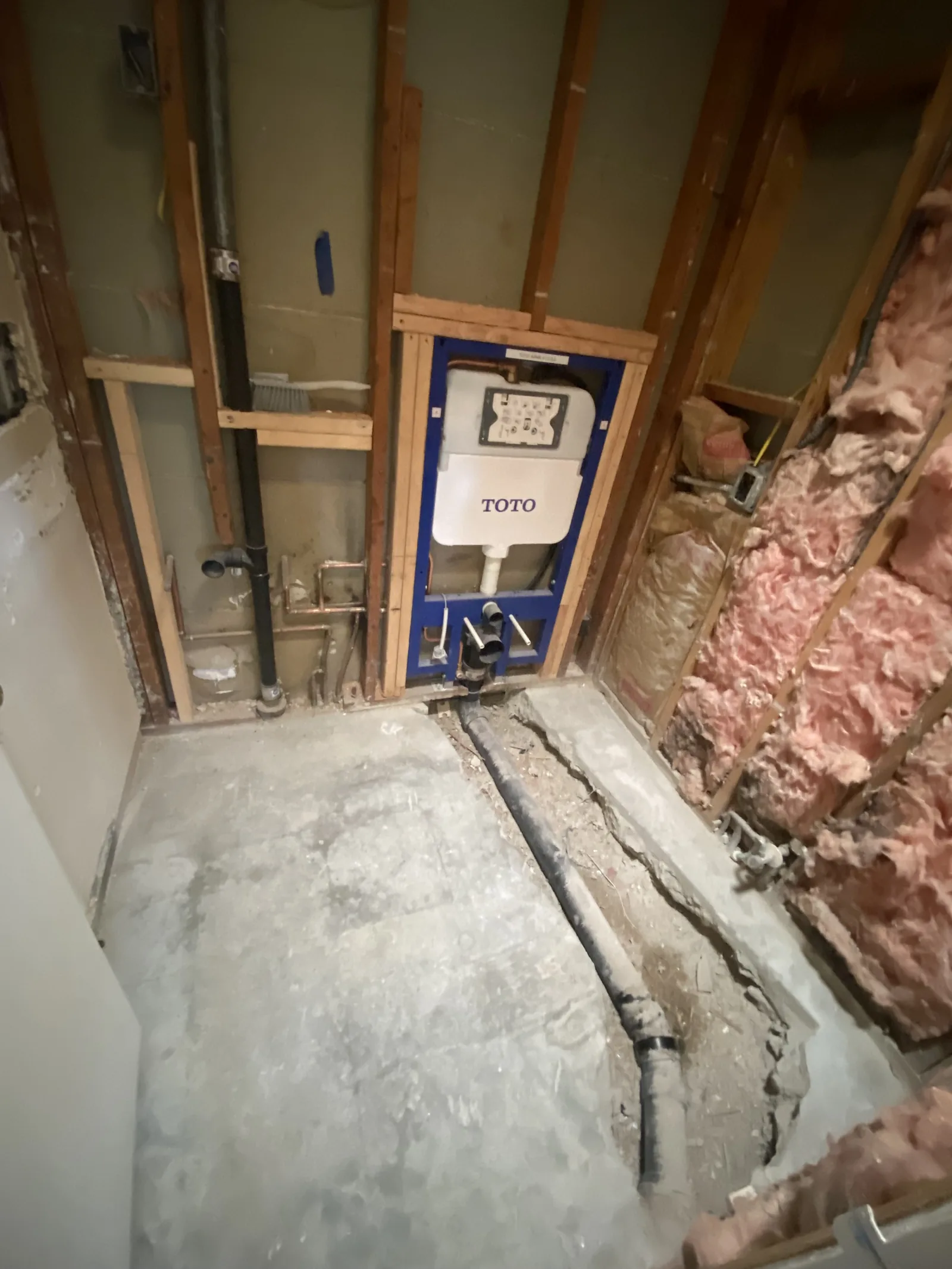 A second concealed carrier frame with a waste pipe running down into a cut trench in the slab floor