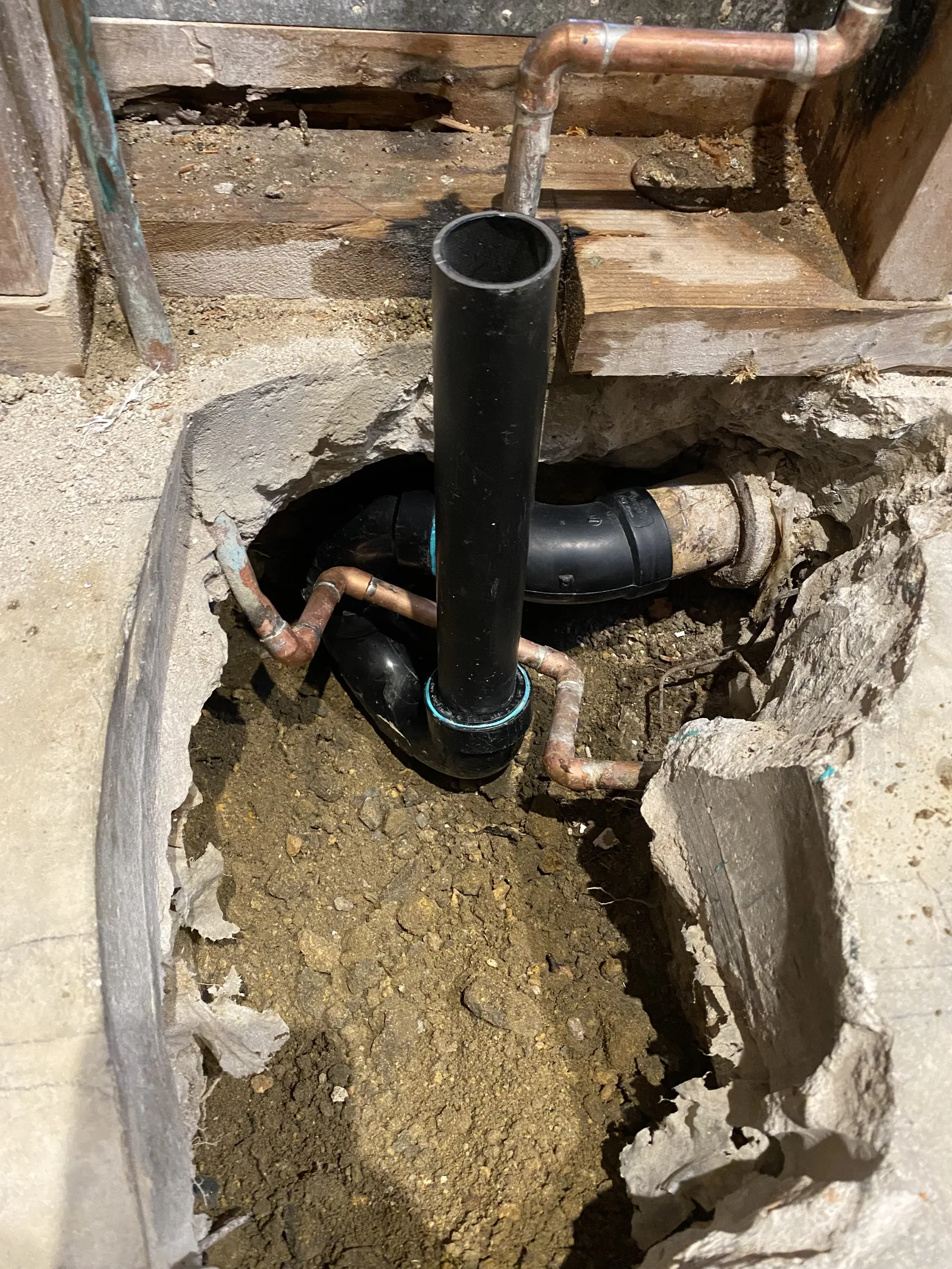 Copper and black ABS pipe fittings joined together inside an opening cut in the concrete slab