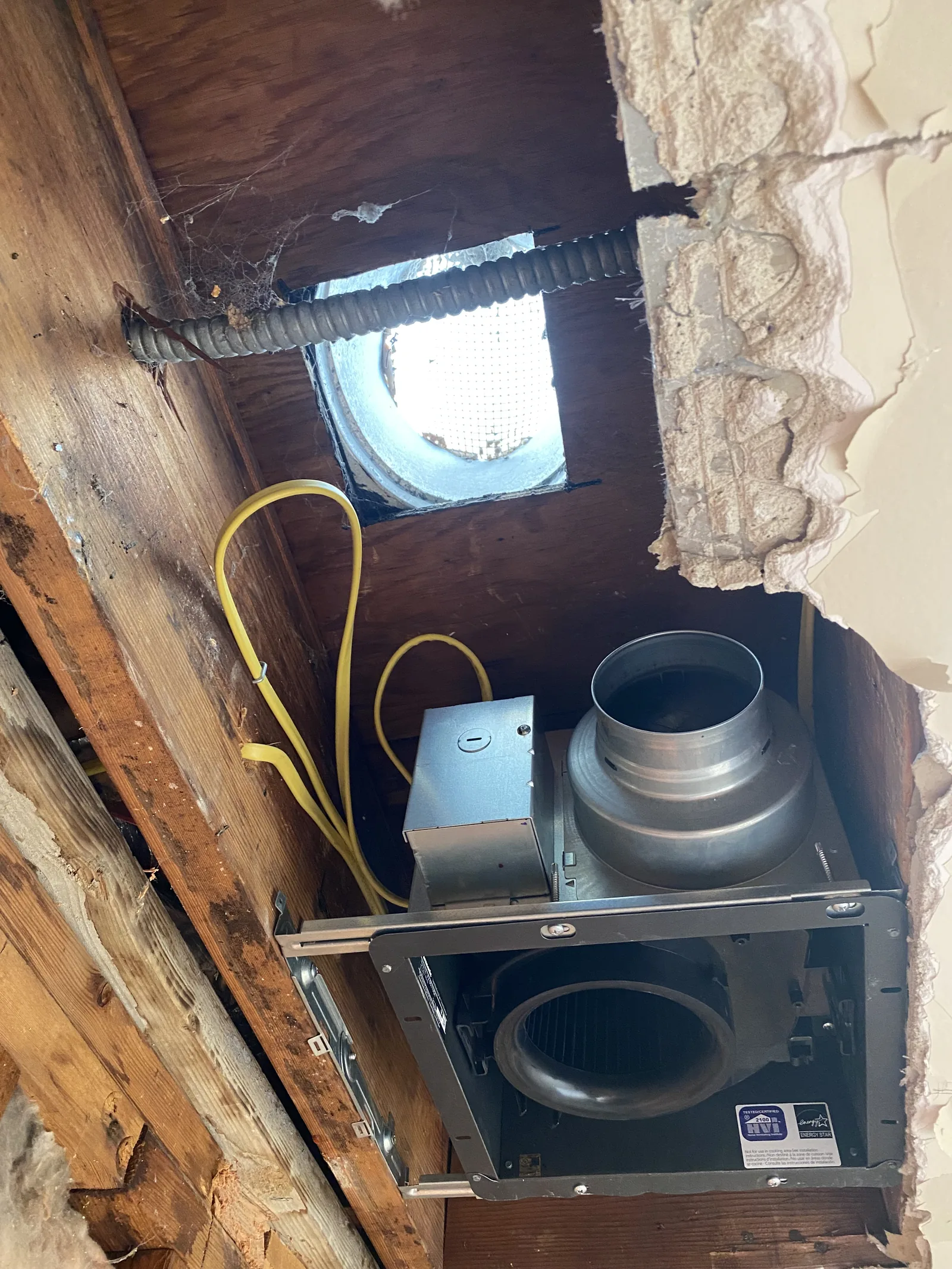 A new bathroom exhaust fan being installed in the attic, with yellow low-voltage wiring run to it