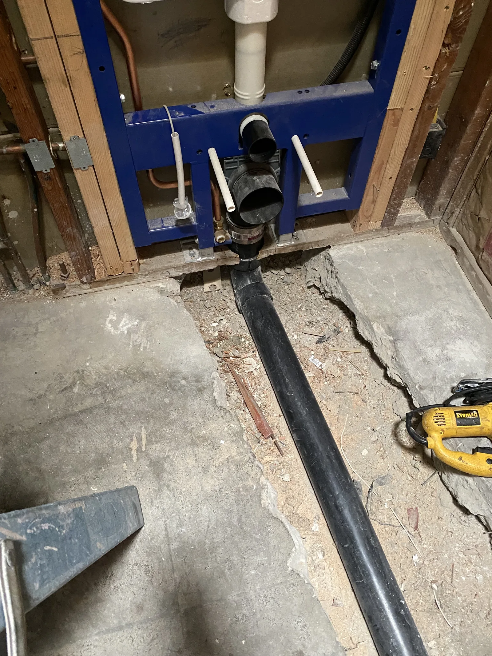 The base of a concealed carrier frame with its waste line running directly into a cut trench in the slab