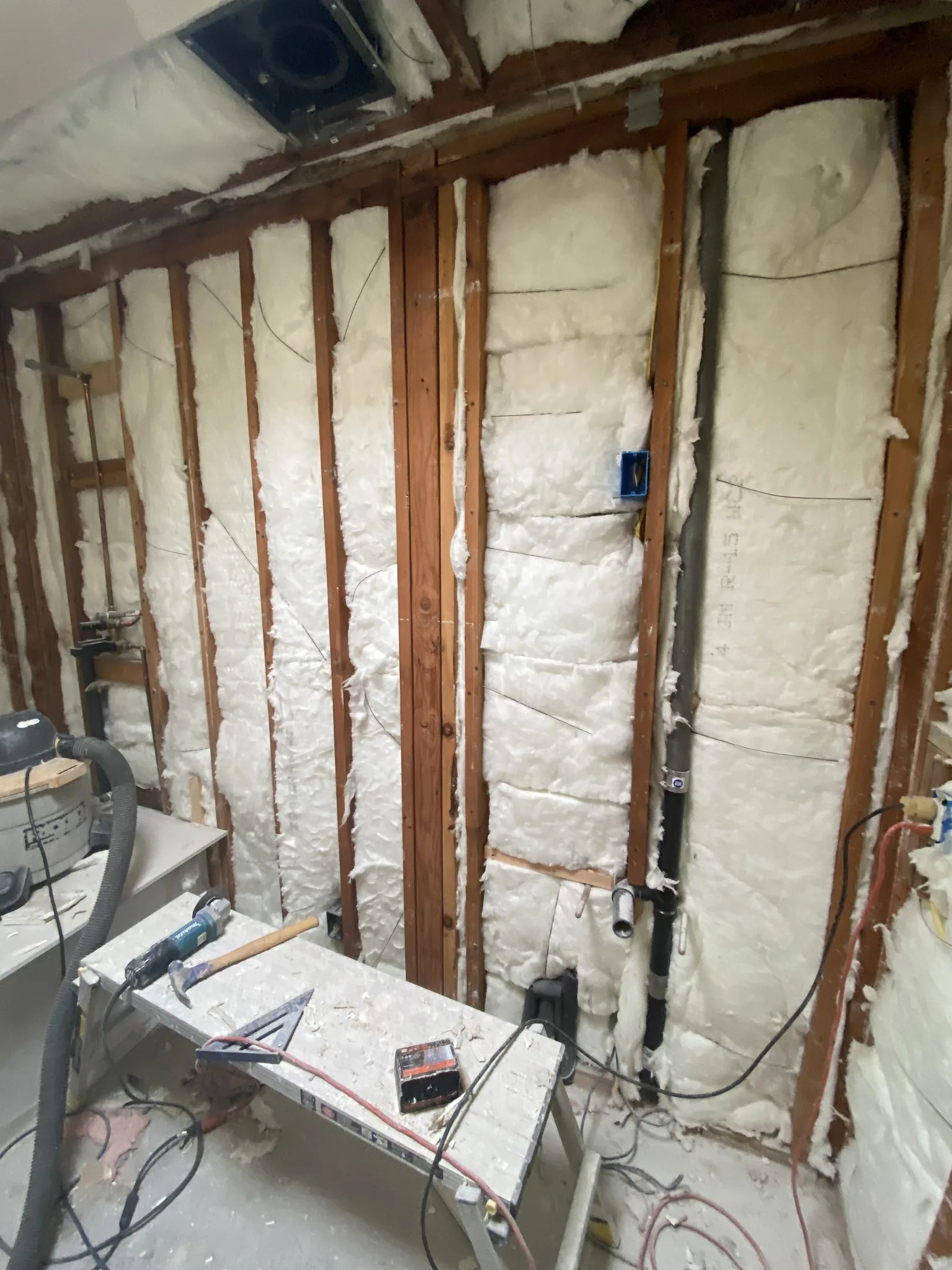 Spray foam insulation filling the wall and ceiling framing of a gutted bathroom, with an electrical box in place