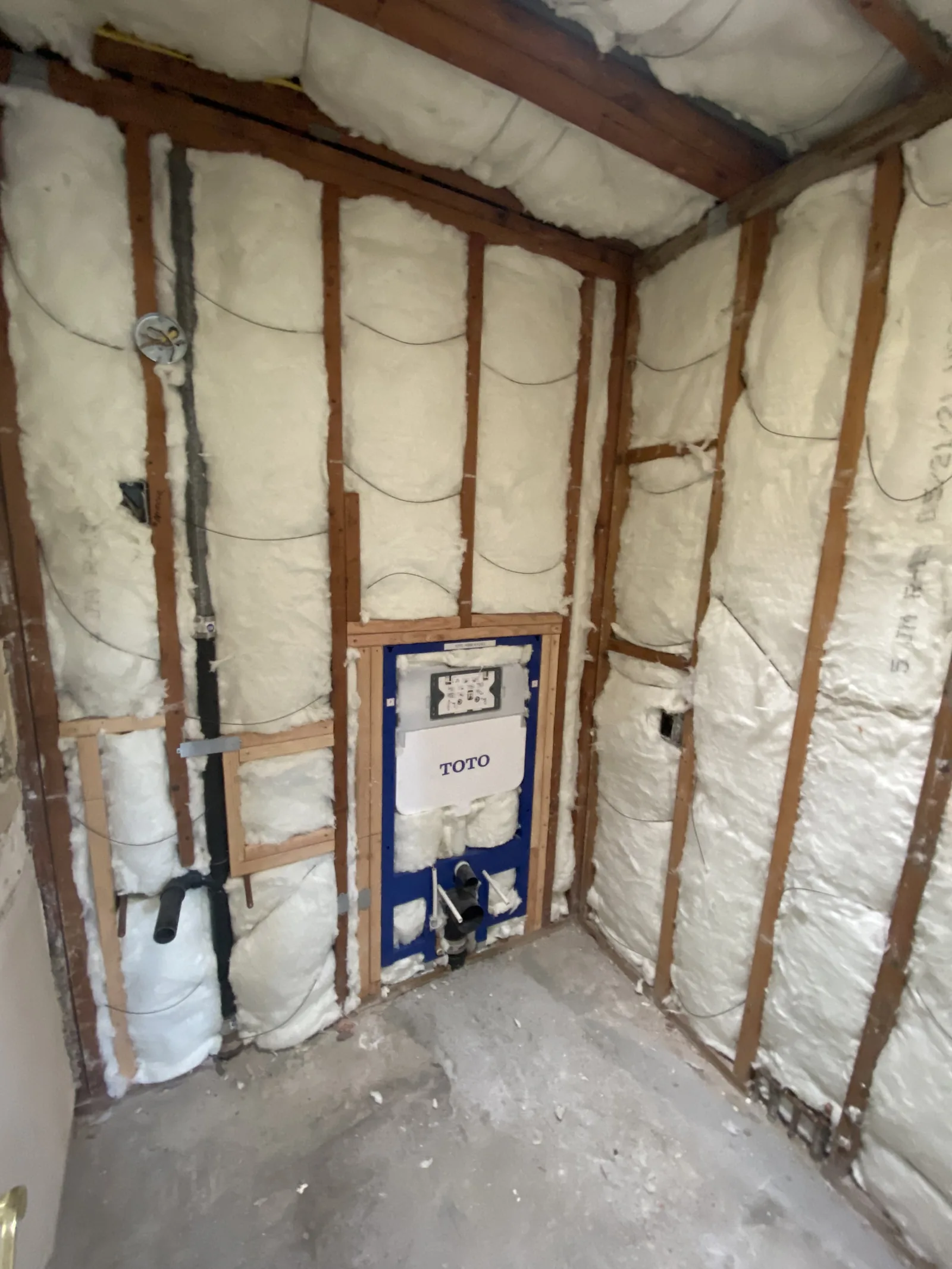 A fully spray-foam-insulated bathroom with a TOTO carrier frame centered in the far wall