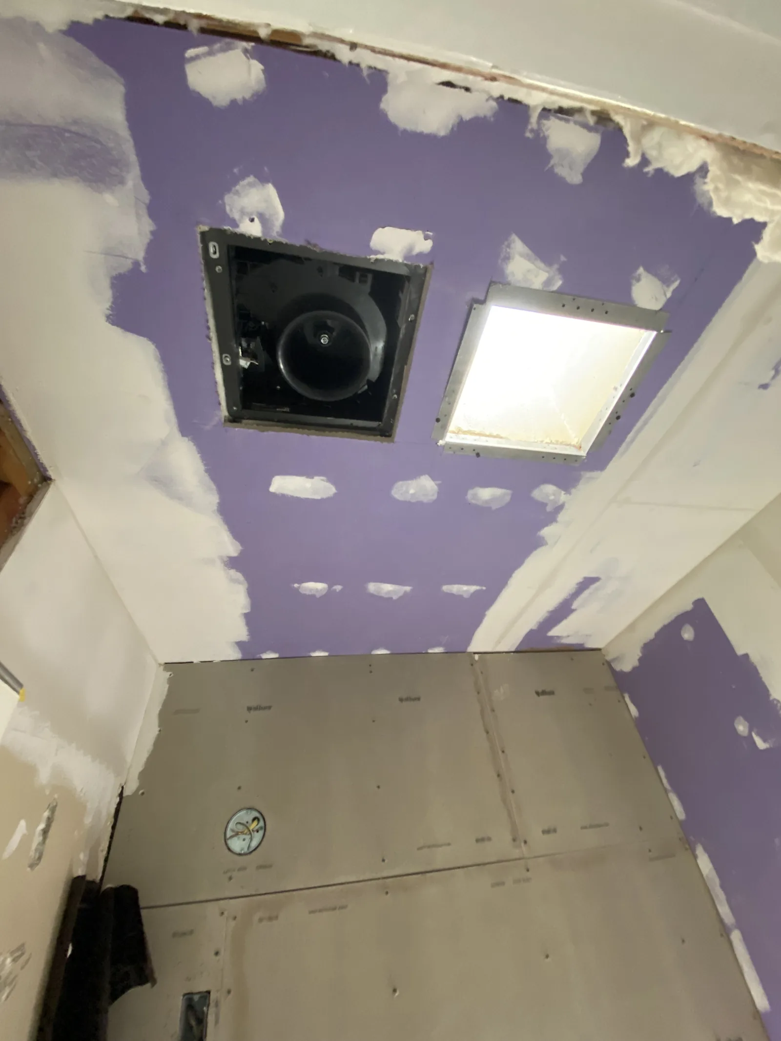 A new skylight installed in a ceiling patched with purple moisture-resistant drywall, with a bath fan nearby