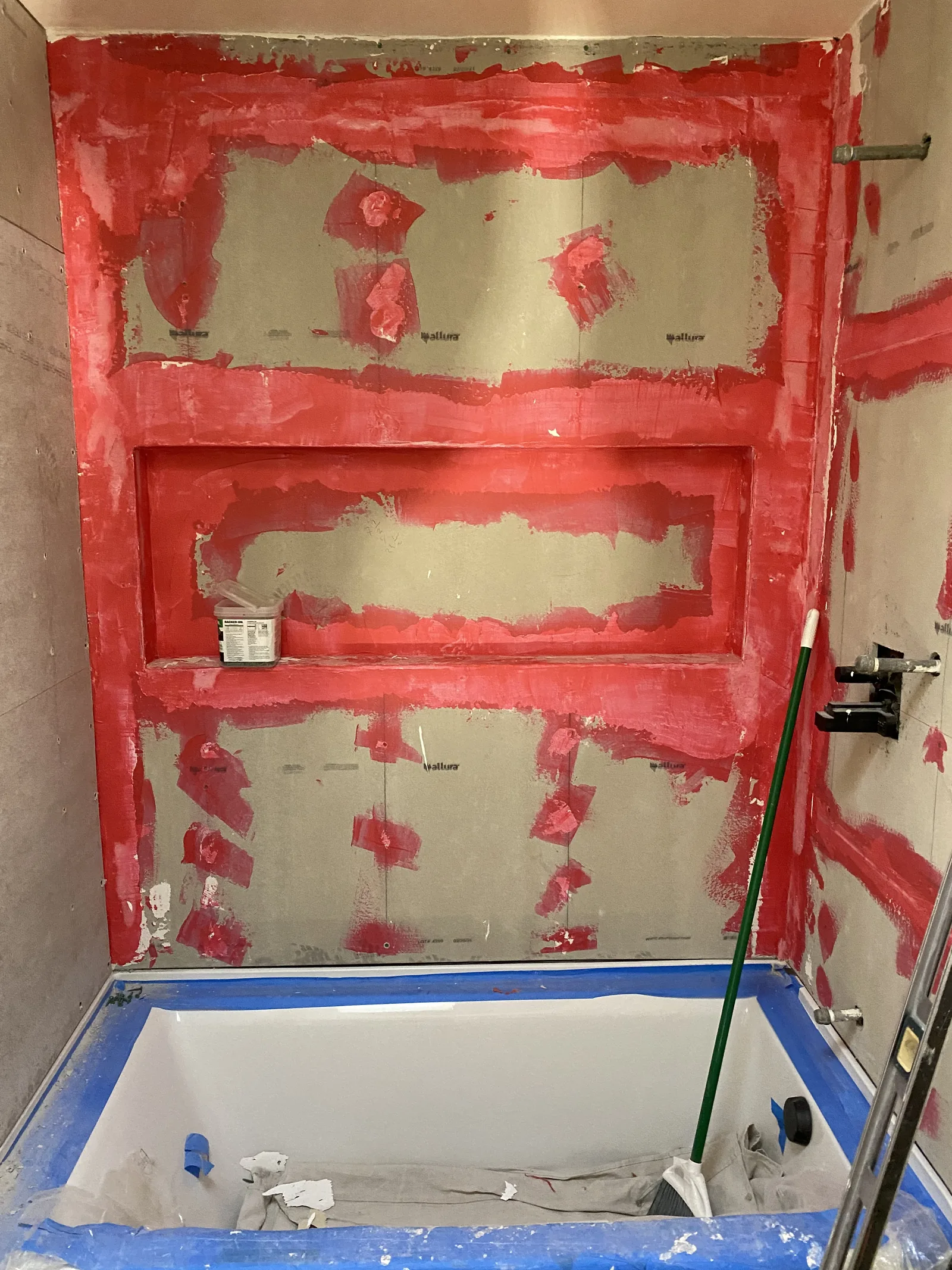 Red waterproofing membrane applied over cement board on a tub surround with a niche, tub protected in plastic