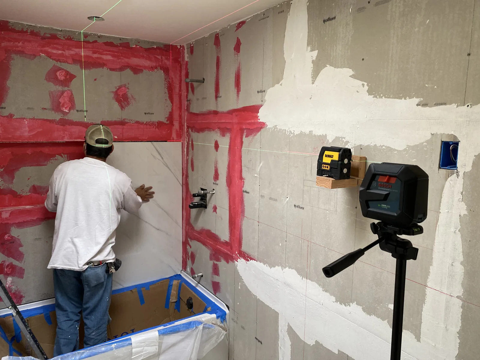 Two laser levels projecting reference lines while a worker sets the first course of large-format tile