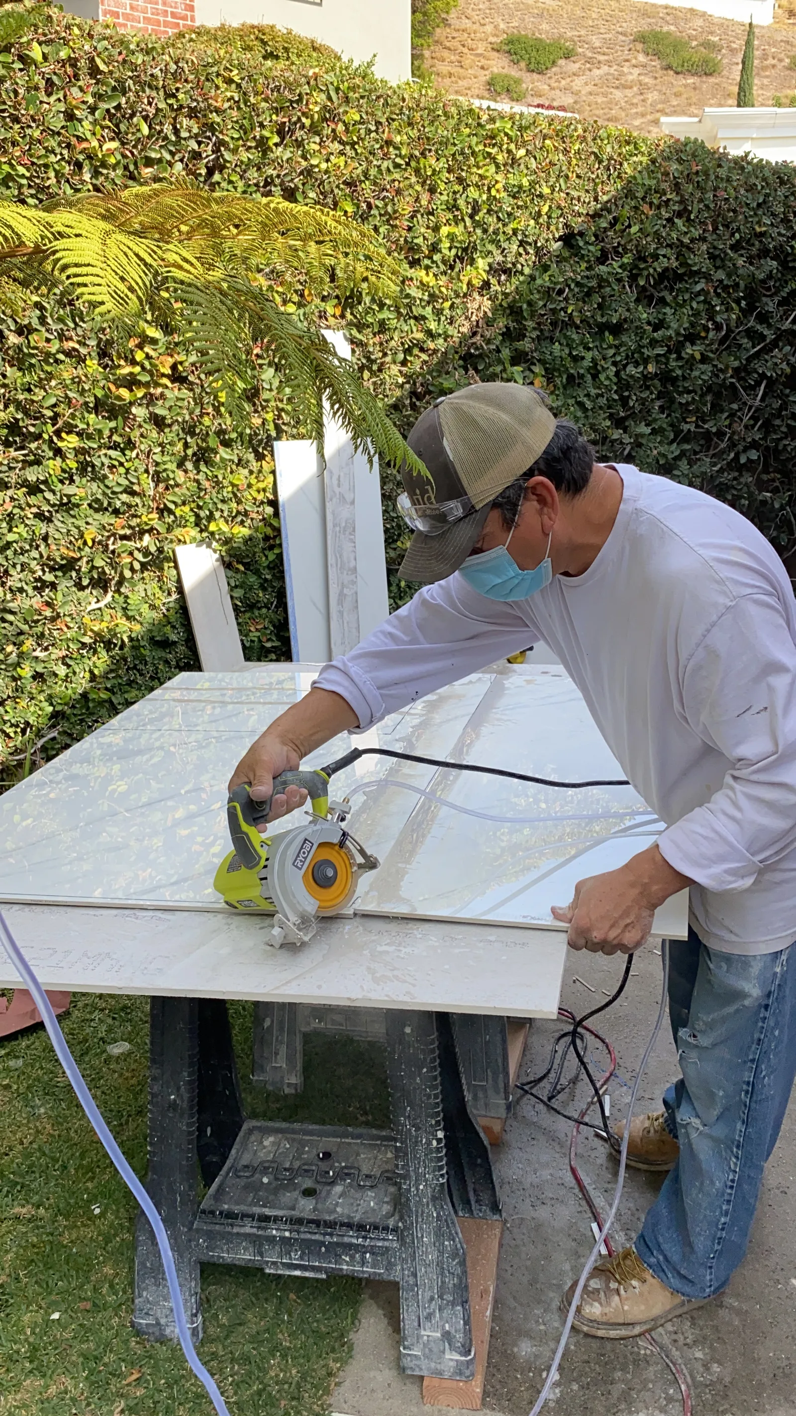A worker cutting a large marble-look tile slab to size outdoors on a wet saw