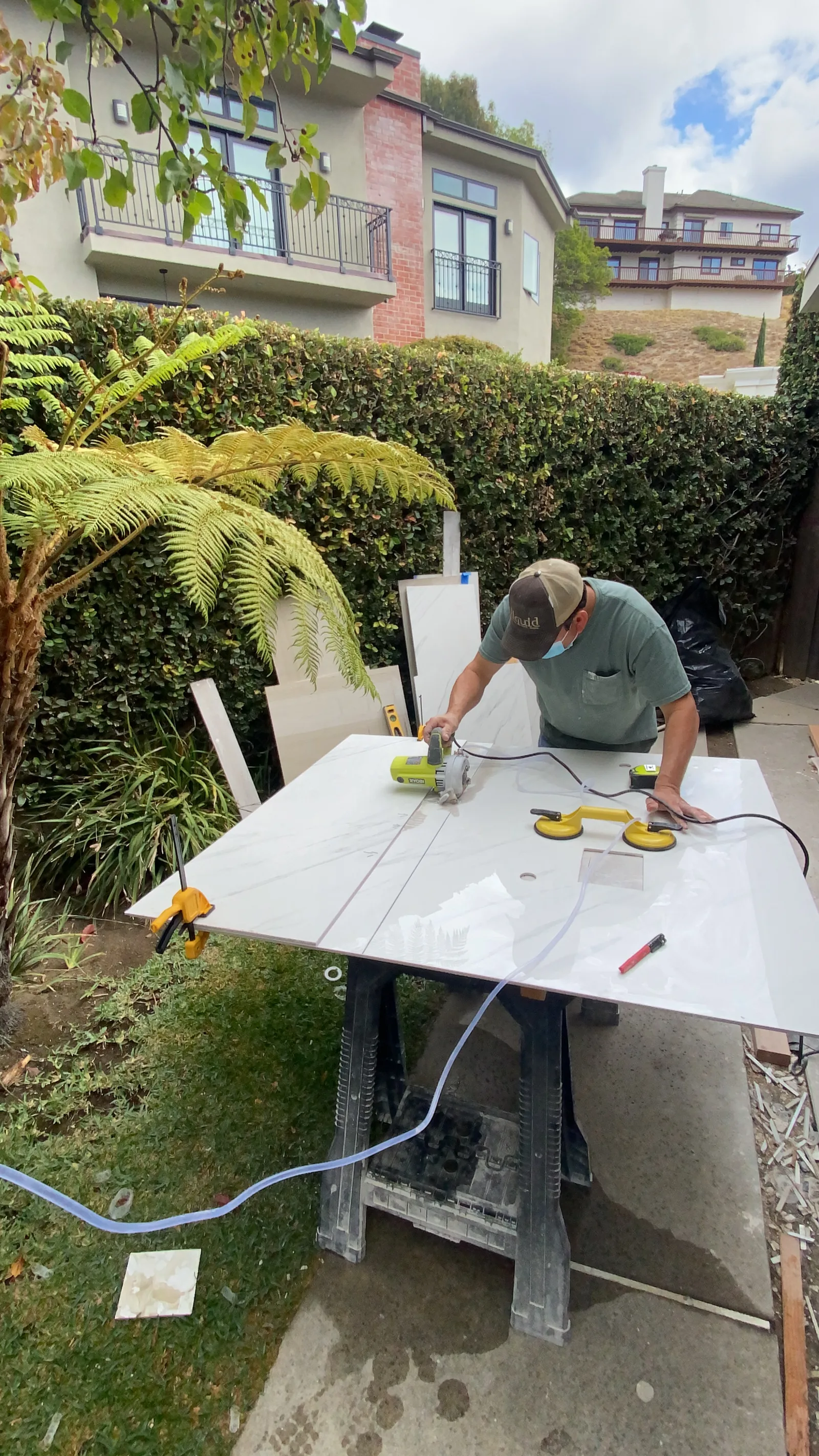 A worker using suction cup handles to carry a large cut tile slab from an outdoor cutting table