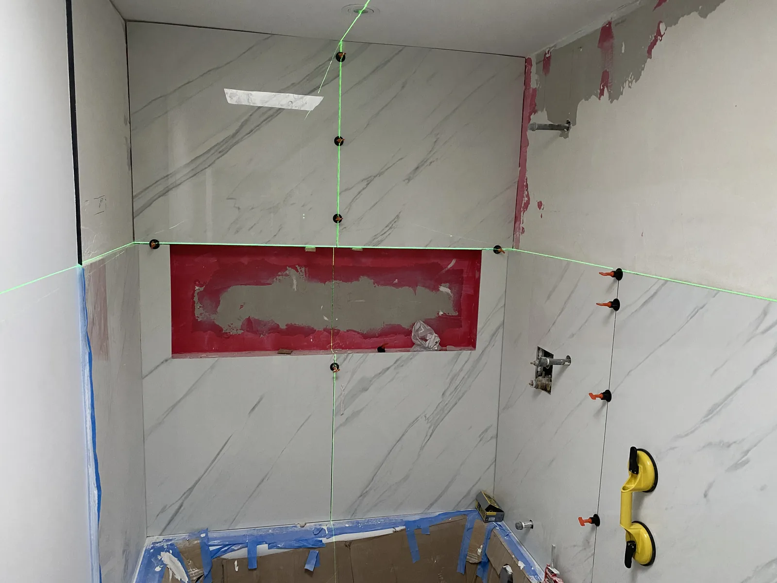 Laser cross-lines guiding tile installation around a partially tiled shower niche