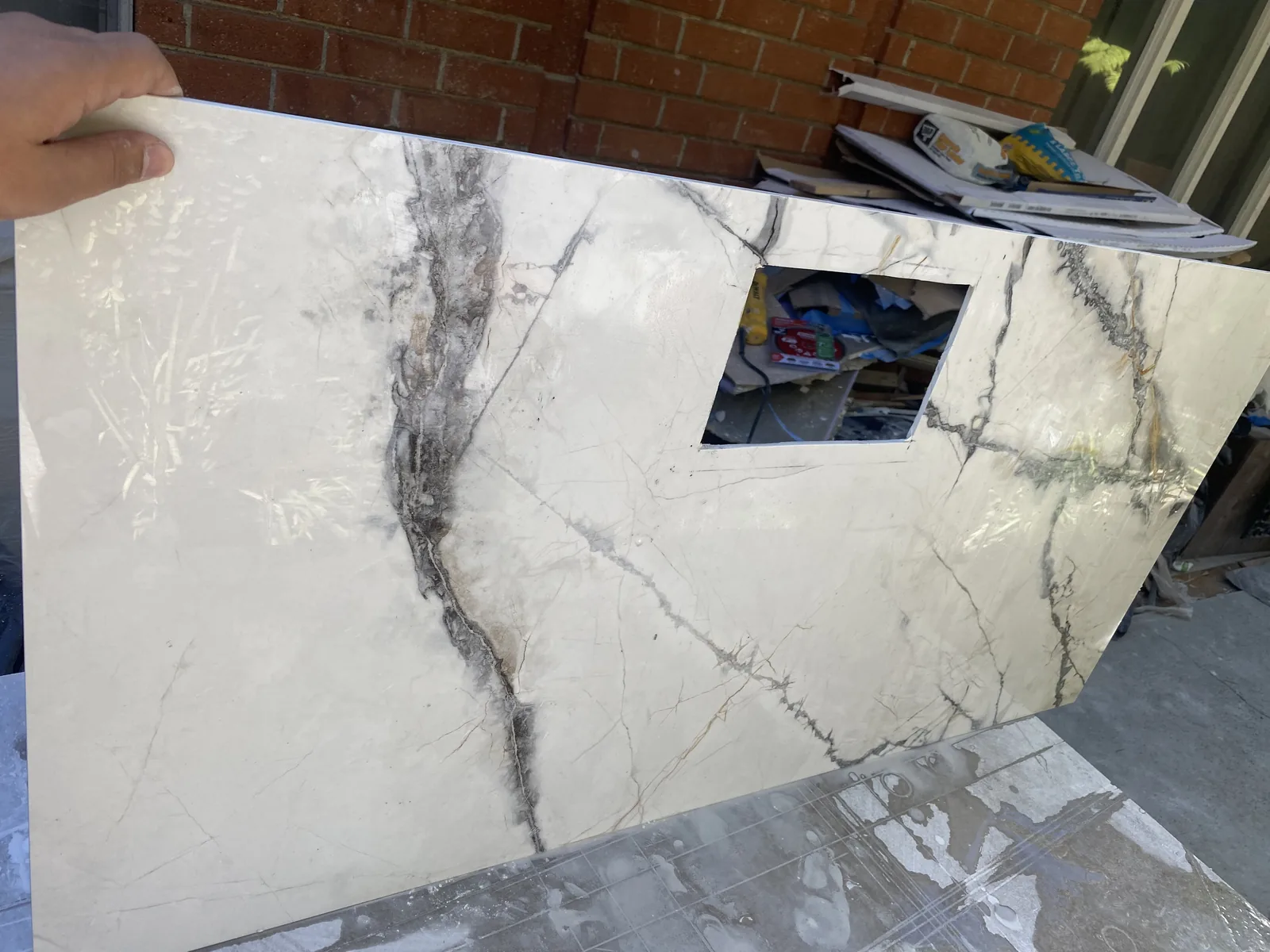 A large tile slab held outdoors with a precise rectangular niche cutout, deep marble veining visible
