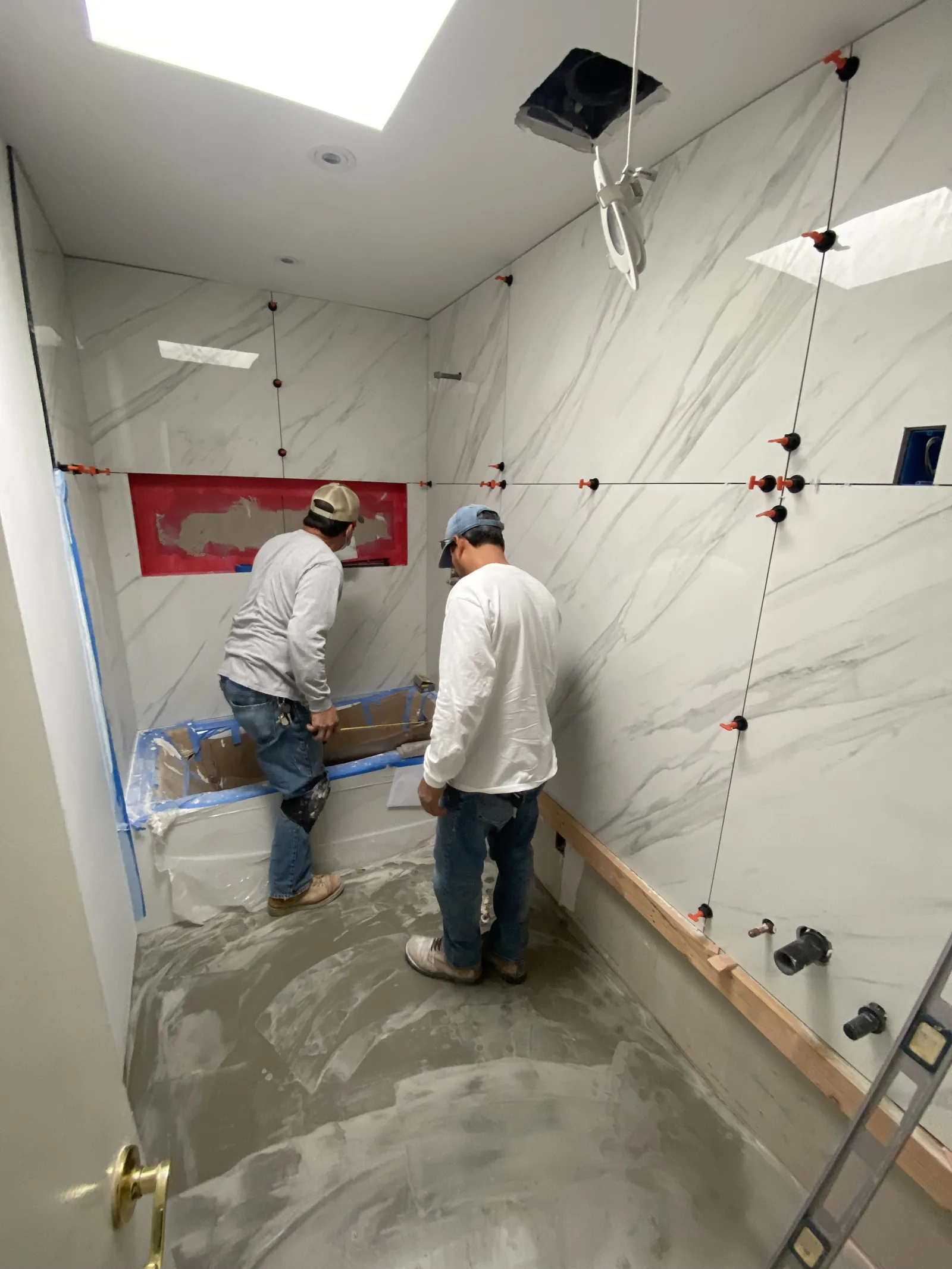 Two workers collaborating on tile installation around a protected tub