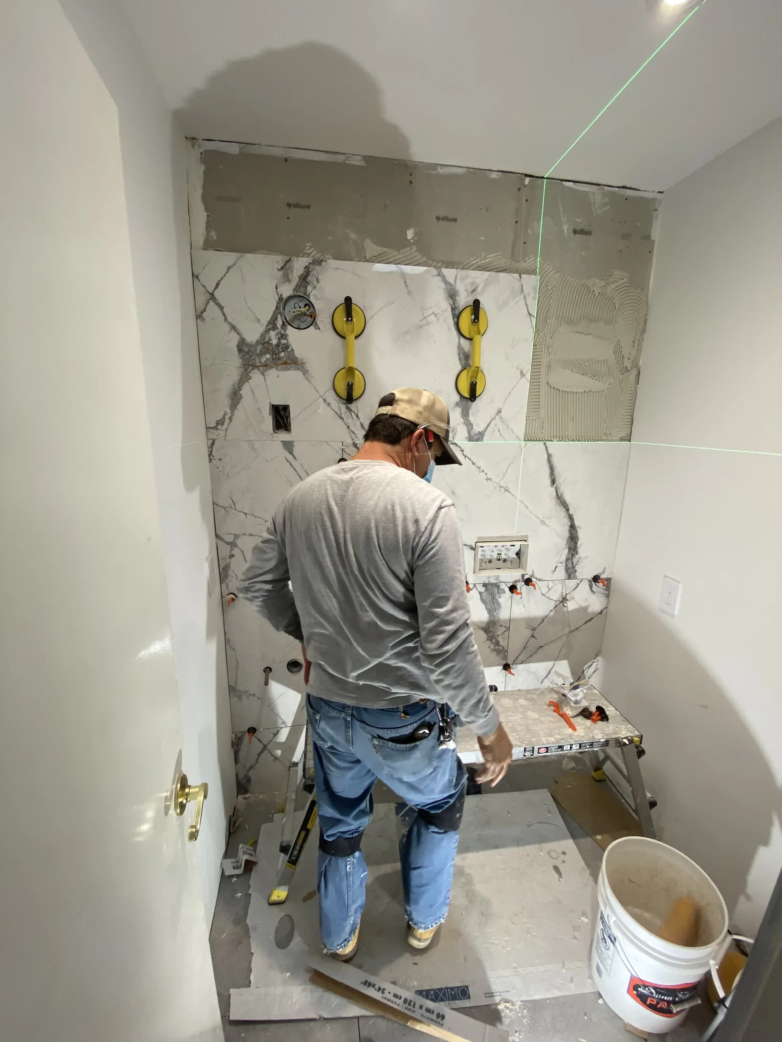 An installer using a laser level to align large-format tile on a bathroom wall