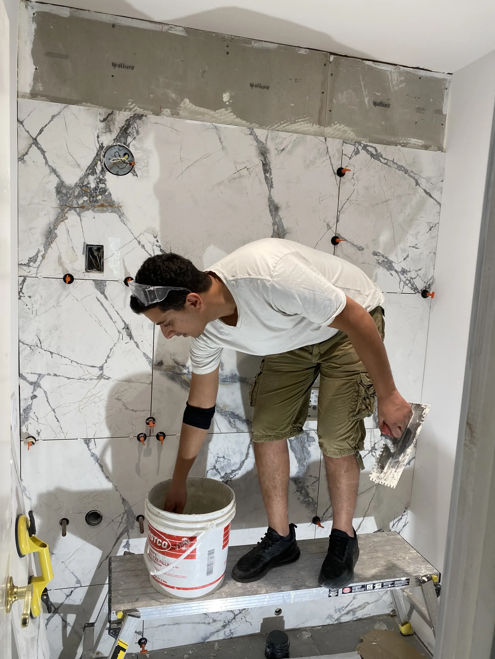 A worker mixing tile mortar in a bucket while standing on a platform in the powder room