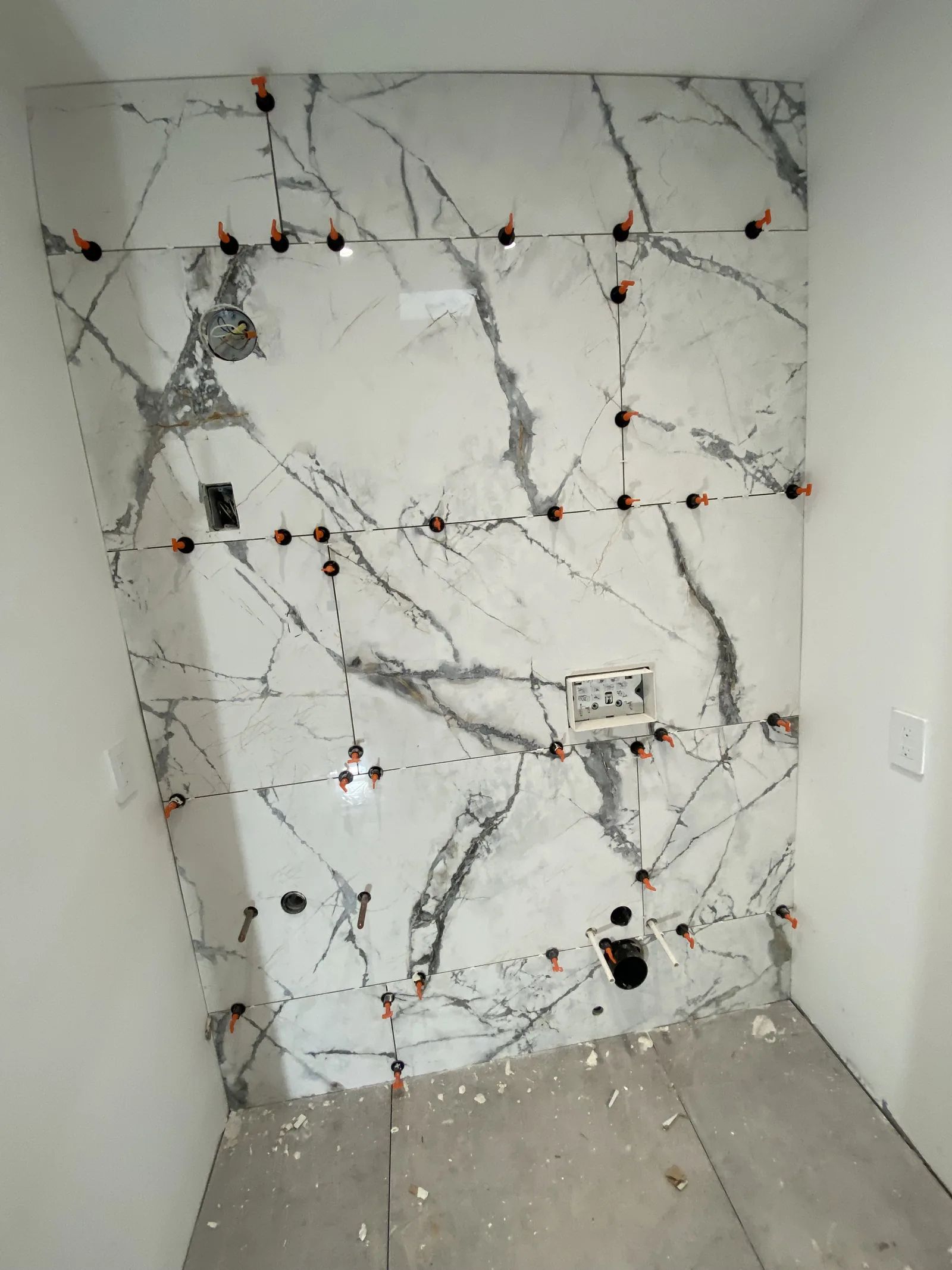 A fully tiled shower alcove nook with toilet rough-in visible at the base of the wall