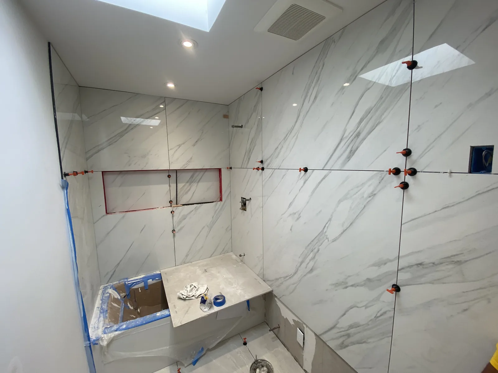 A nearly complete tub and shower room with tile on every wall and a built-in stone bench seat