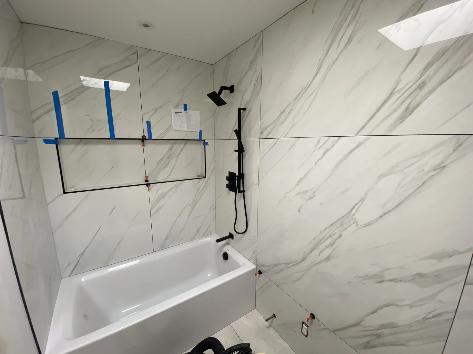A tub and black shower valve set into a finished large-format tile surround