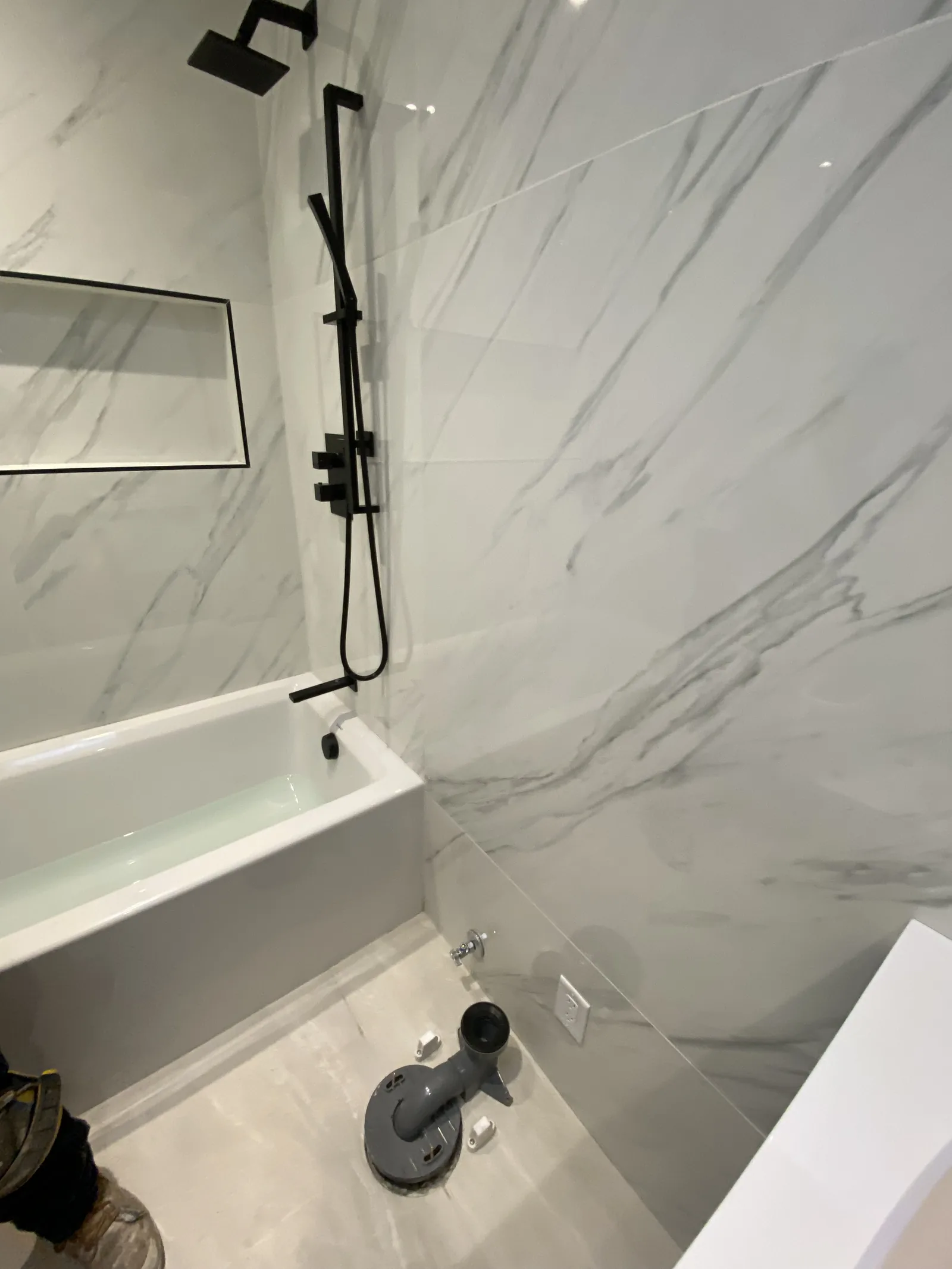 A near-finished tub and shower with black hardware, the tub filled with water, toilet flange visible on the floor