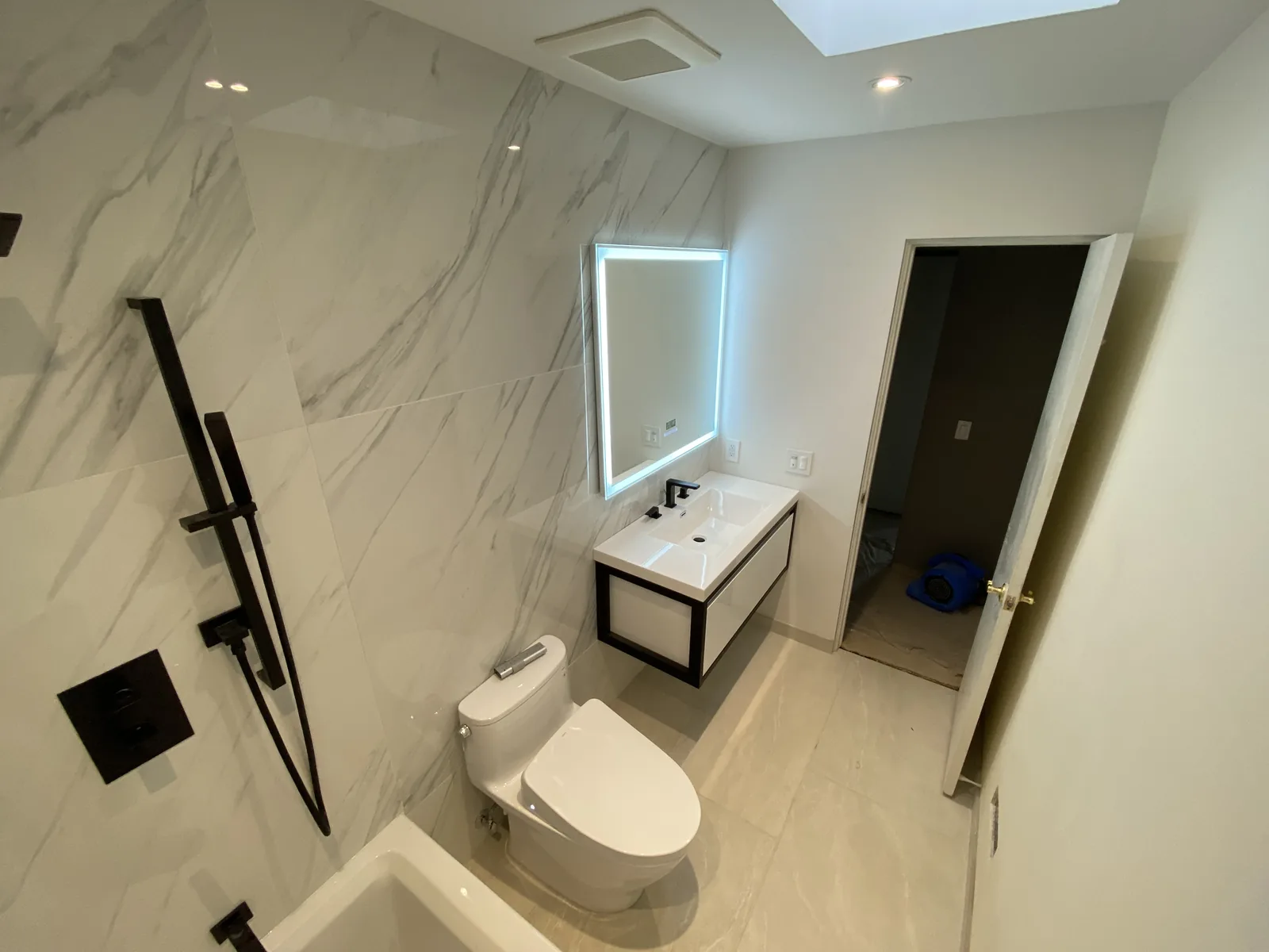 The finished bathroom seen from the doorway, with the vanity, mirror, and tub all visible together