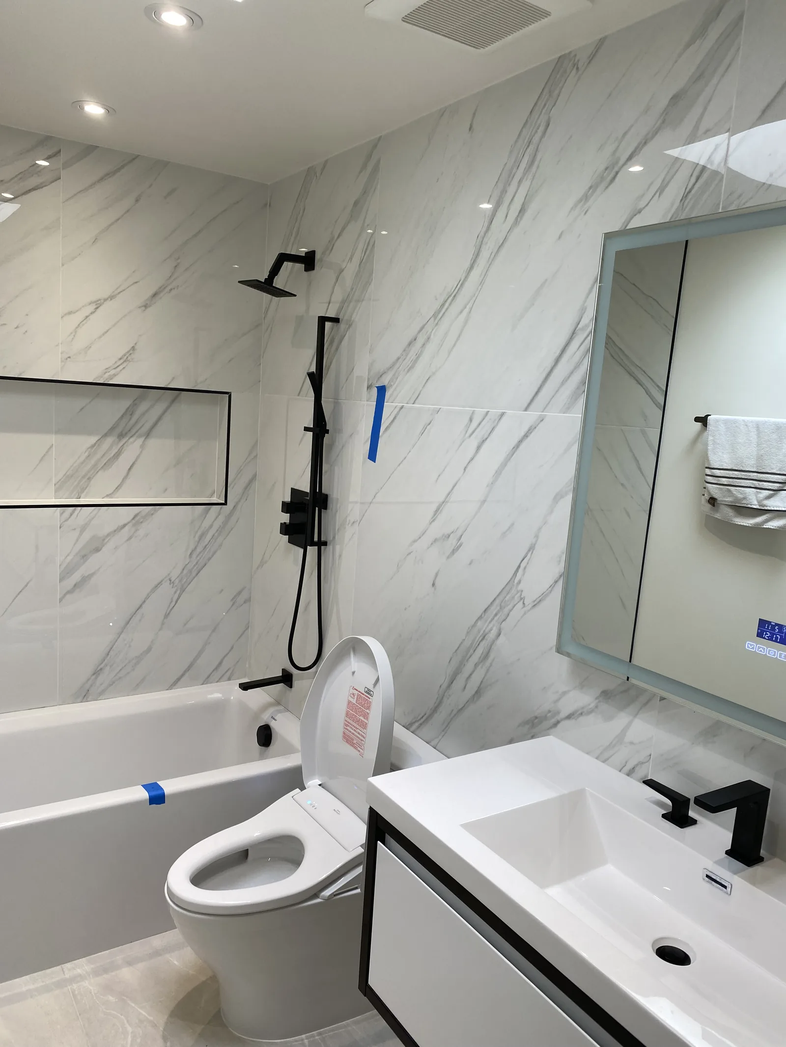 The finished bathroom with the toilet lid open showing the bidet control panel, tub and vanity beyond