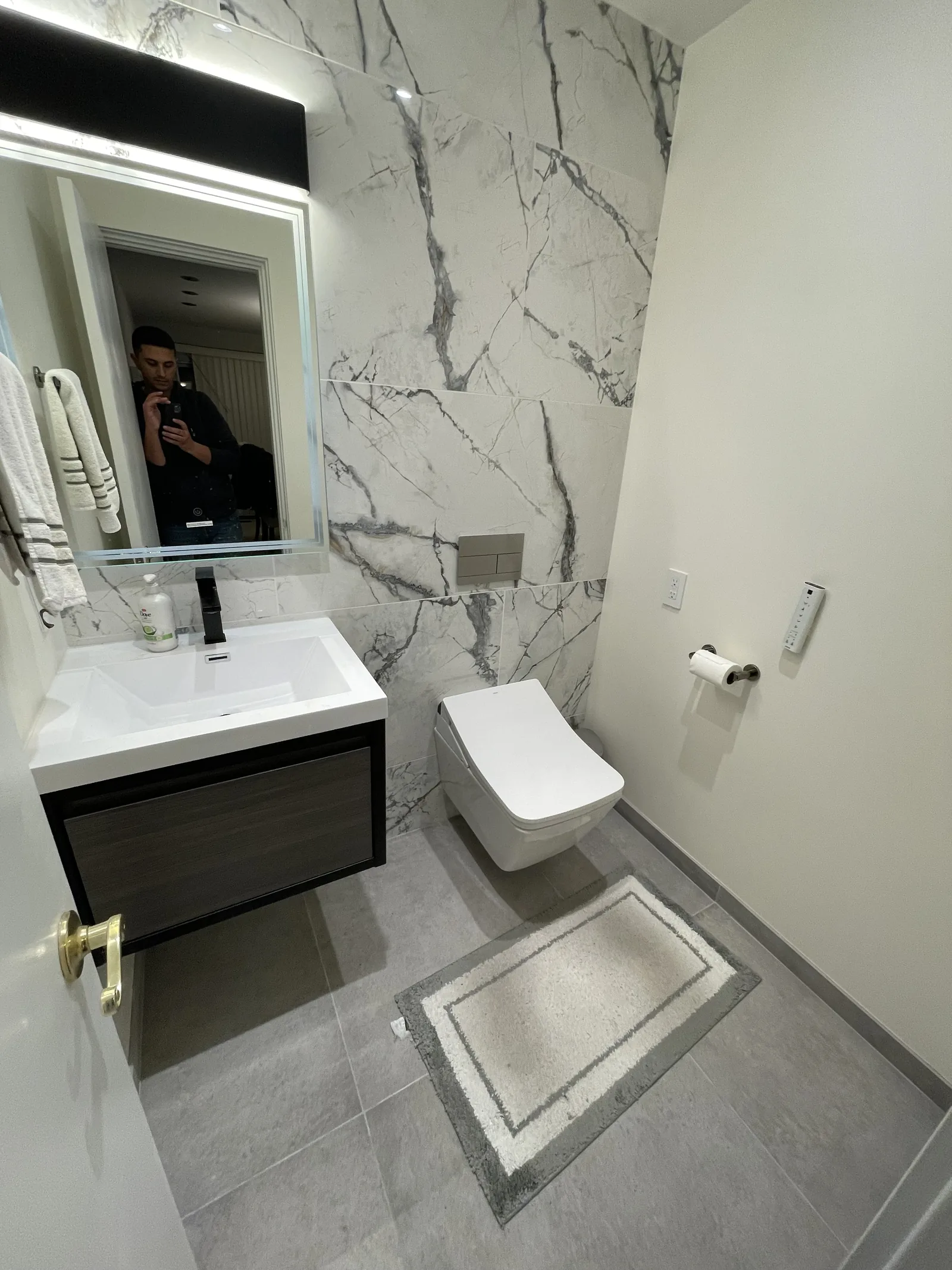 The finished powder room with a floating vanity, backlit mirror, and wall-mounted toilet against floor-to-ceiling tile