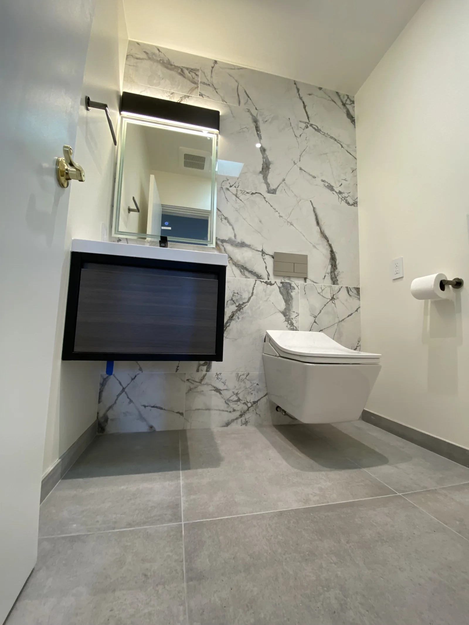 The completed powder room with floor tile installed, toilet paper holder mounted, and the vanity in place