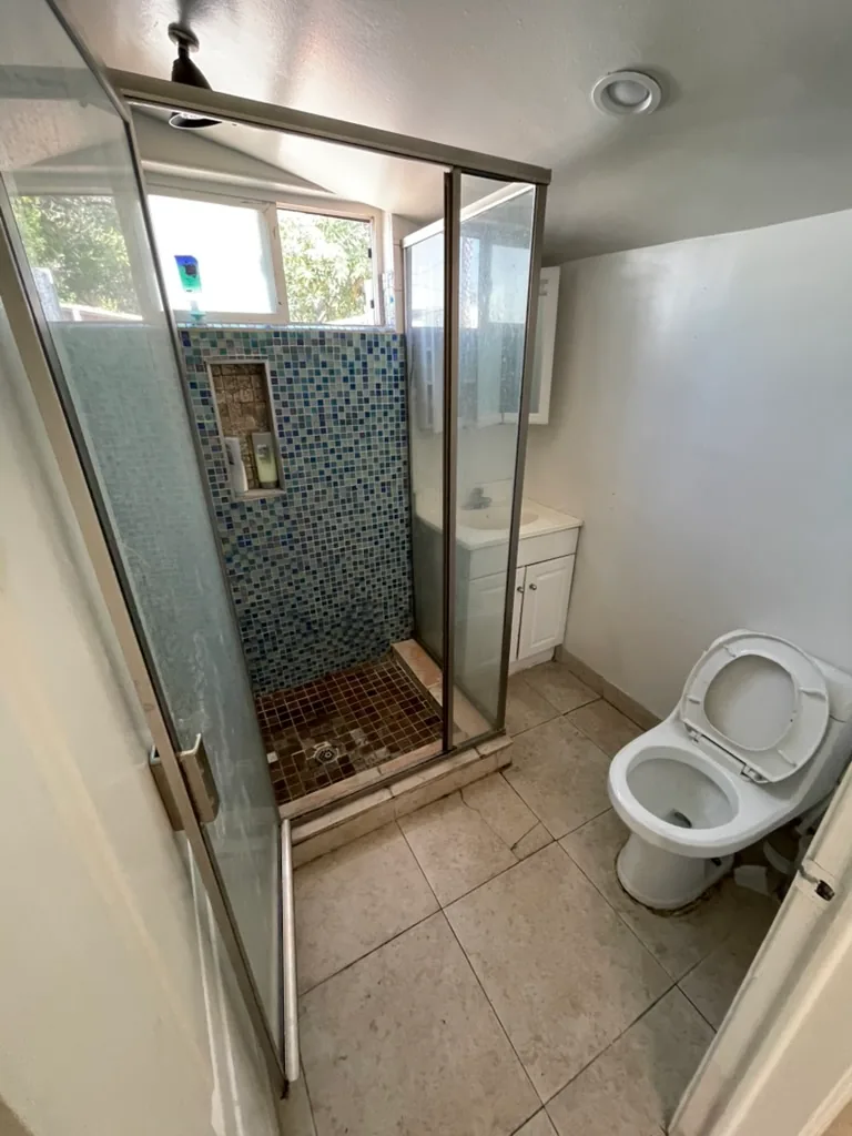 The original bathroom with a framed glass shower in blue mosaic tile, a white vanity and a toilet