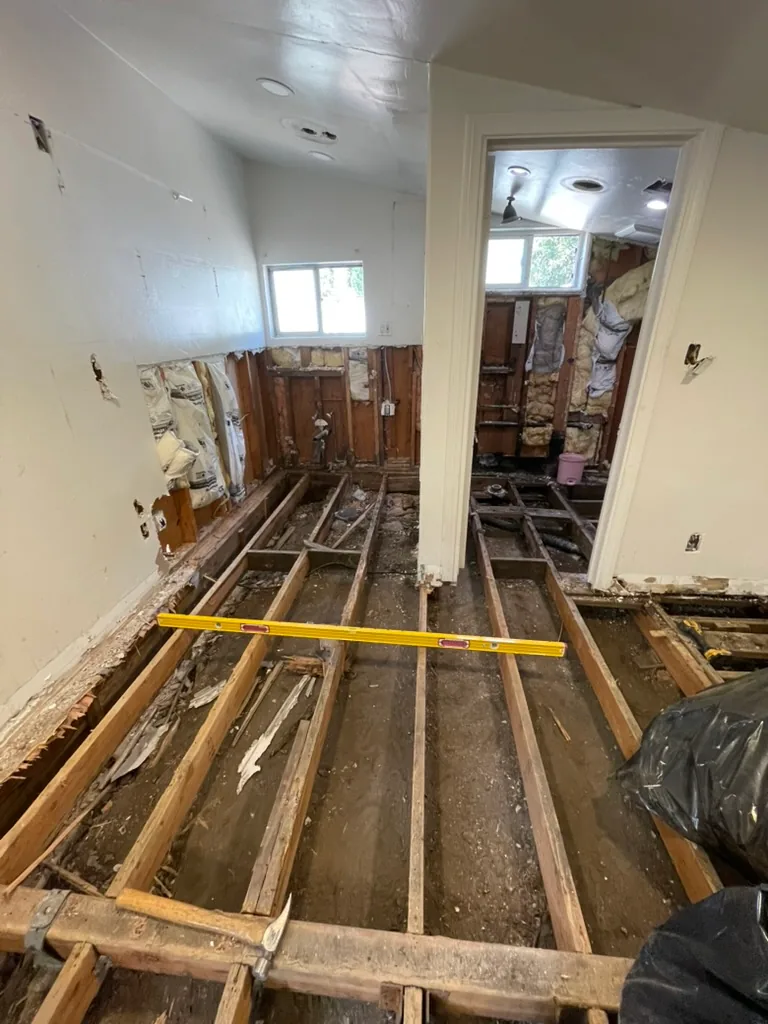 The main room with its floor removed and a yellow level laid across the old joists over soil