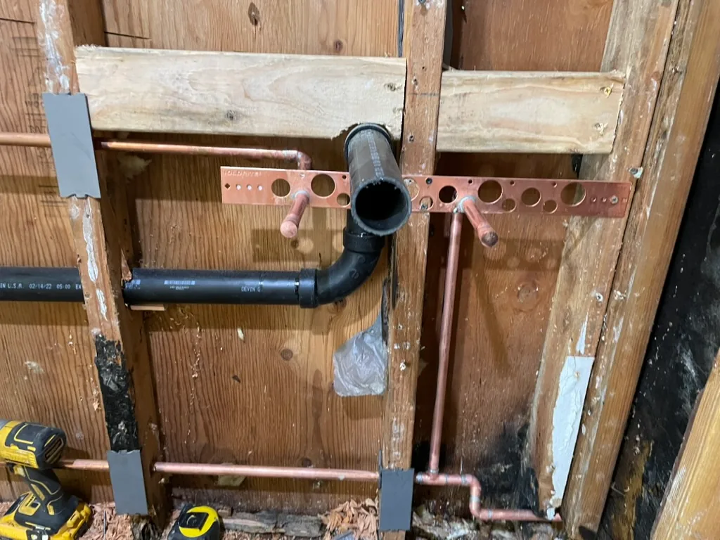 New copper supply stubs on a copper bracket and a new black drain line in an open wall