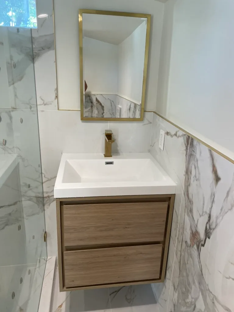 A wall-hung wood-tone vanity with a white sink top, a brass faucet and a brass-framed mirror