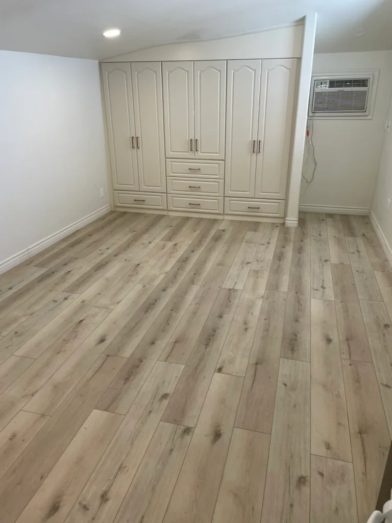 Finished built-in wardrobes with drawers beside a wall air conditioner, over wood-look flooring