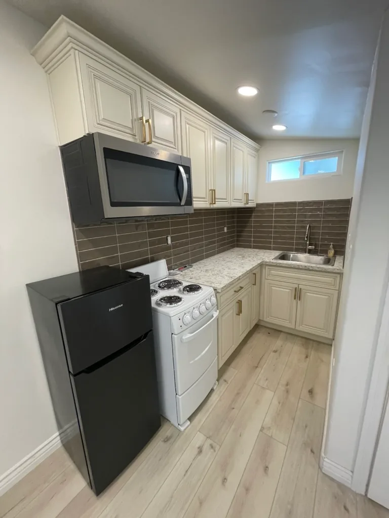 The finished kitchen with cream raised-panel cabinets, a speckled counter and a dark tile backsplash