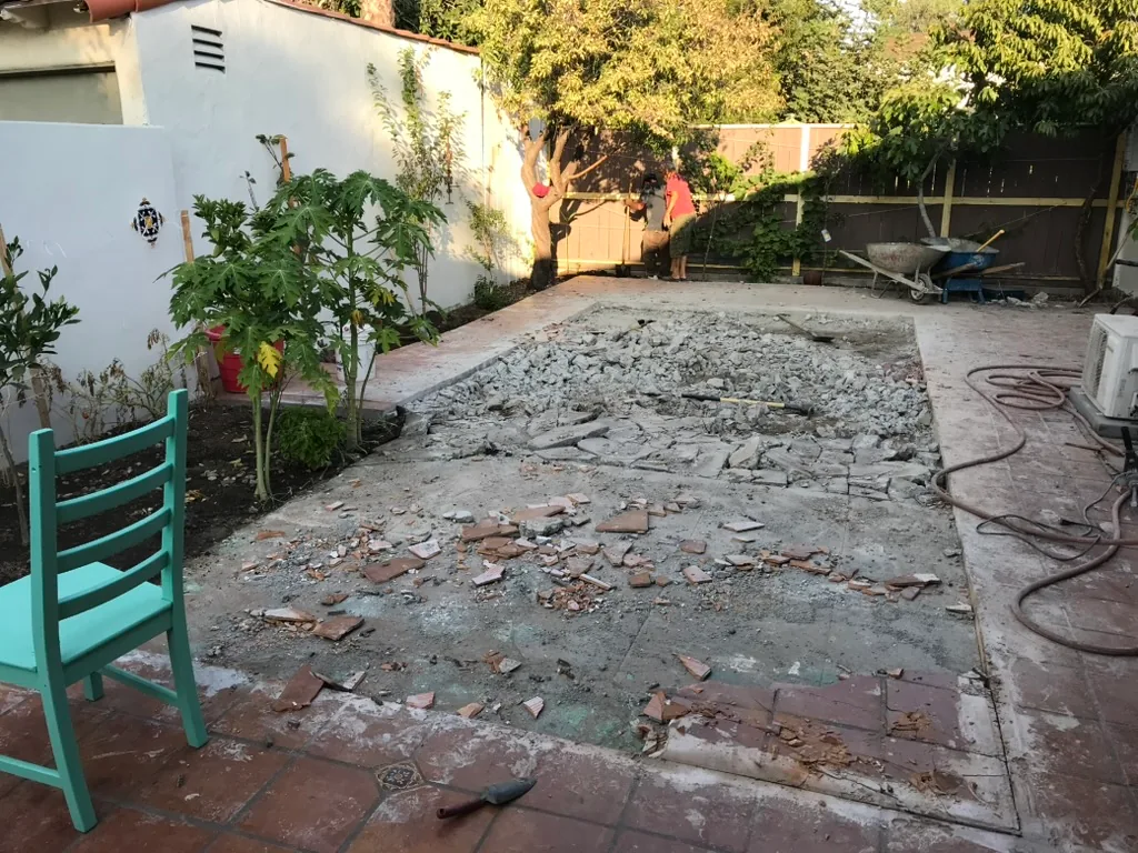 Broken concrete across the middle of a terracotta-tiled patio, between a white wall and the house