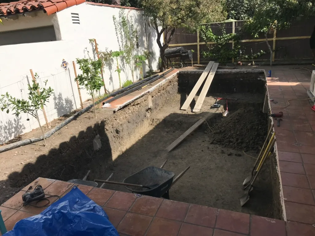 A deepening excavation in the patio with a wheelbarrow inside it
