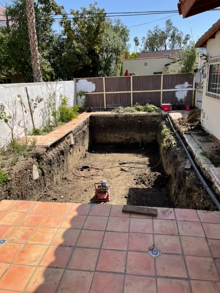 A red plate compactor on the soil floor of the pool excavation