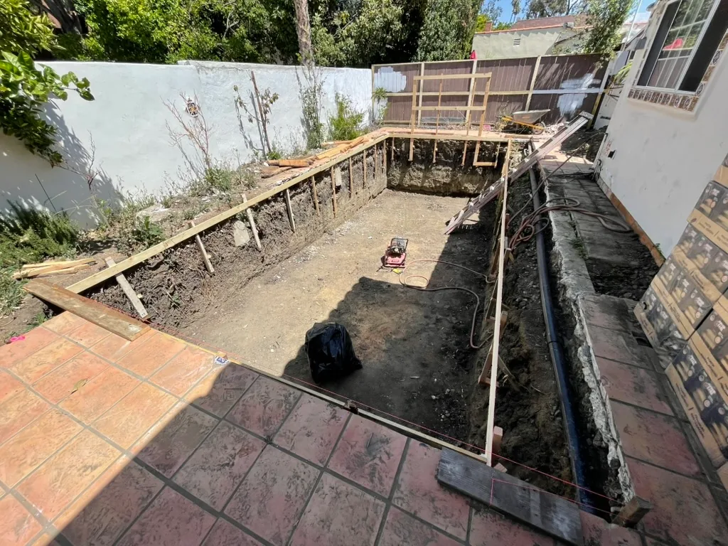 Wood forms set around the pool excavation, with a trench along the house wall