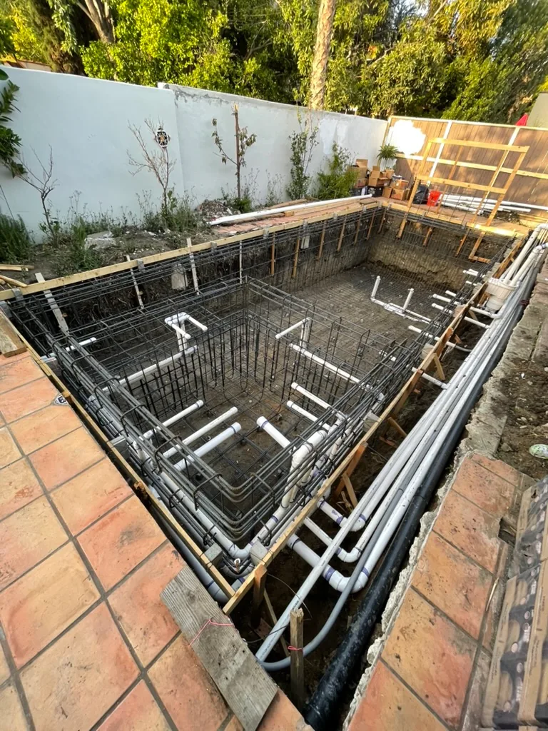 White plumbing lines run through the rebar of the pool and spa