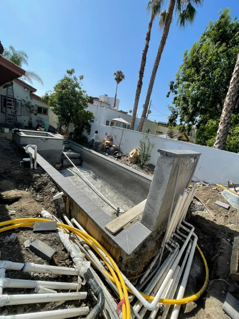 A yellow gas line and white pipes laid in a trench beside the pool shell